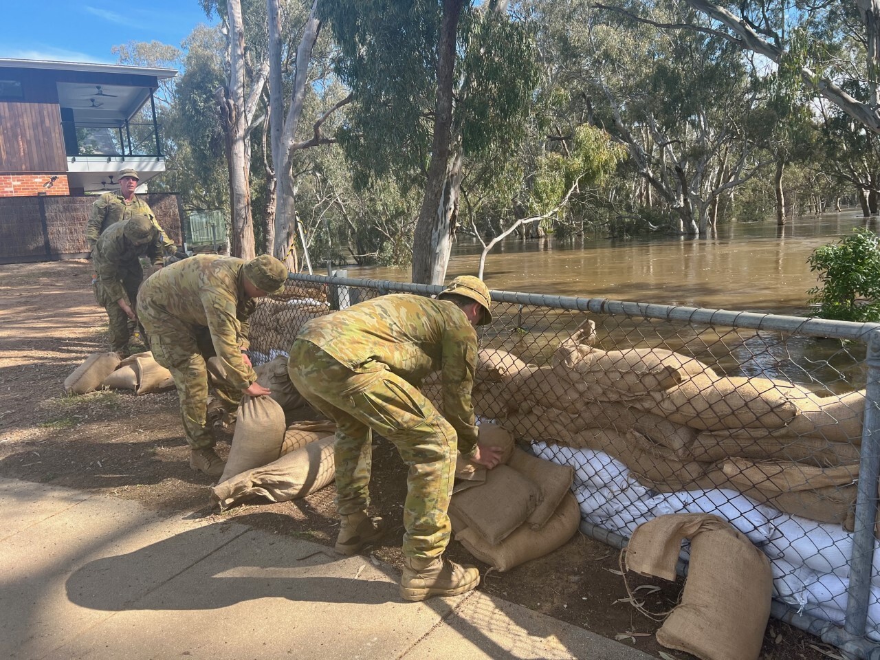 Military personnel place sandbags in a levee