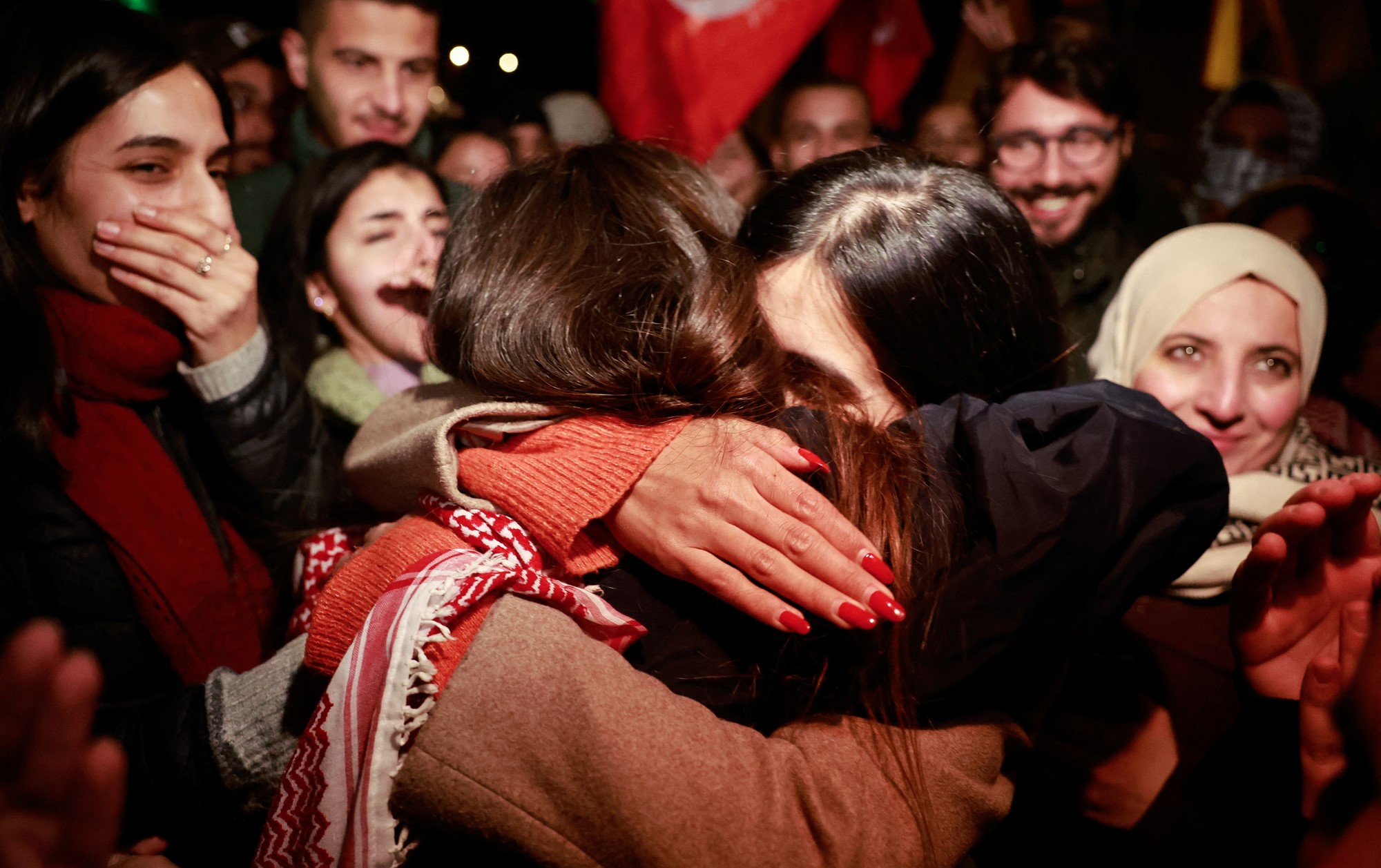 A close up of two women embracing, among a crowd of other people celebrating and smiling