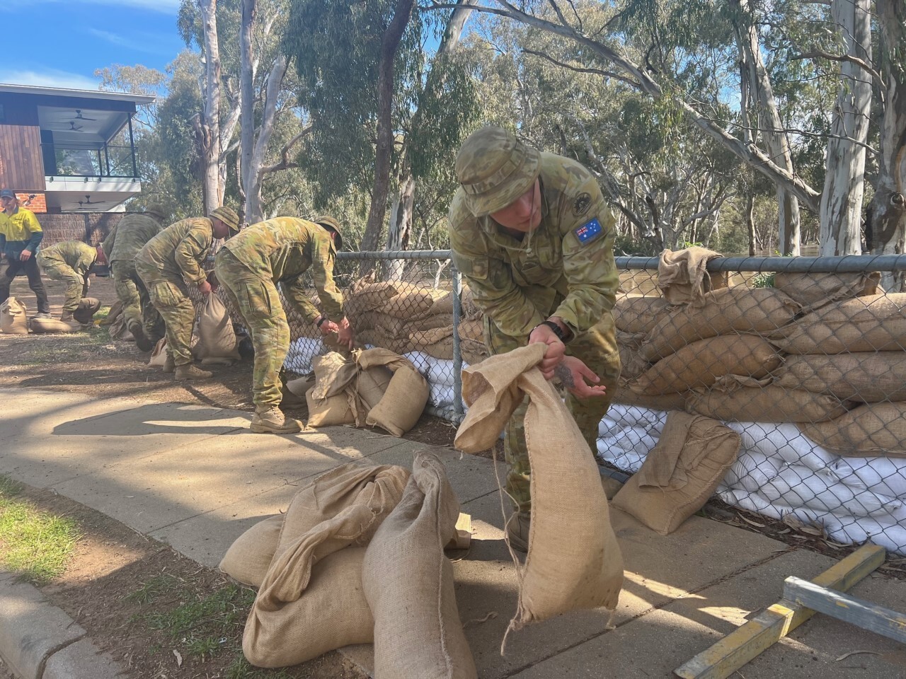 Military personnel place sandbags in a levee