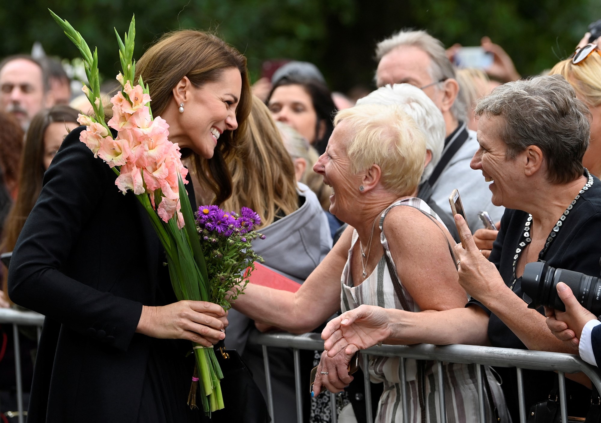 Kate smiles widely at a woman who hands her pink flowers.
