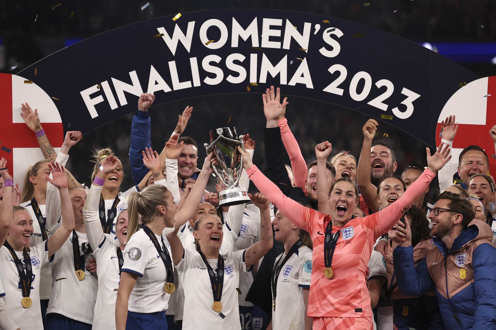 The England women's team chears holding a trophy under teh Women's Finalissima 2023 banner. 