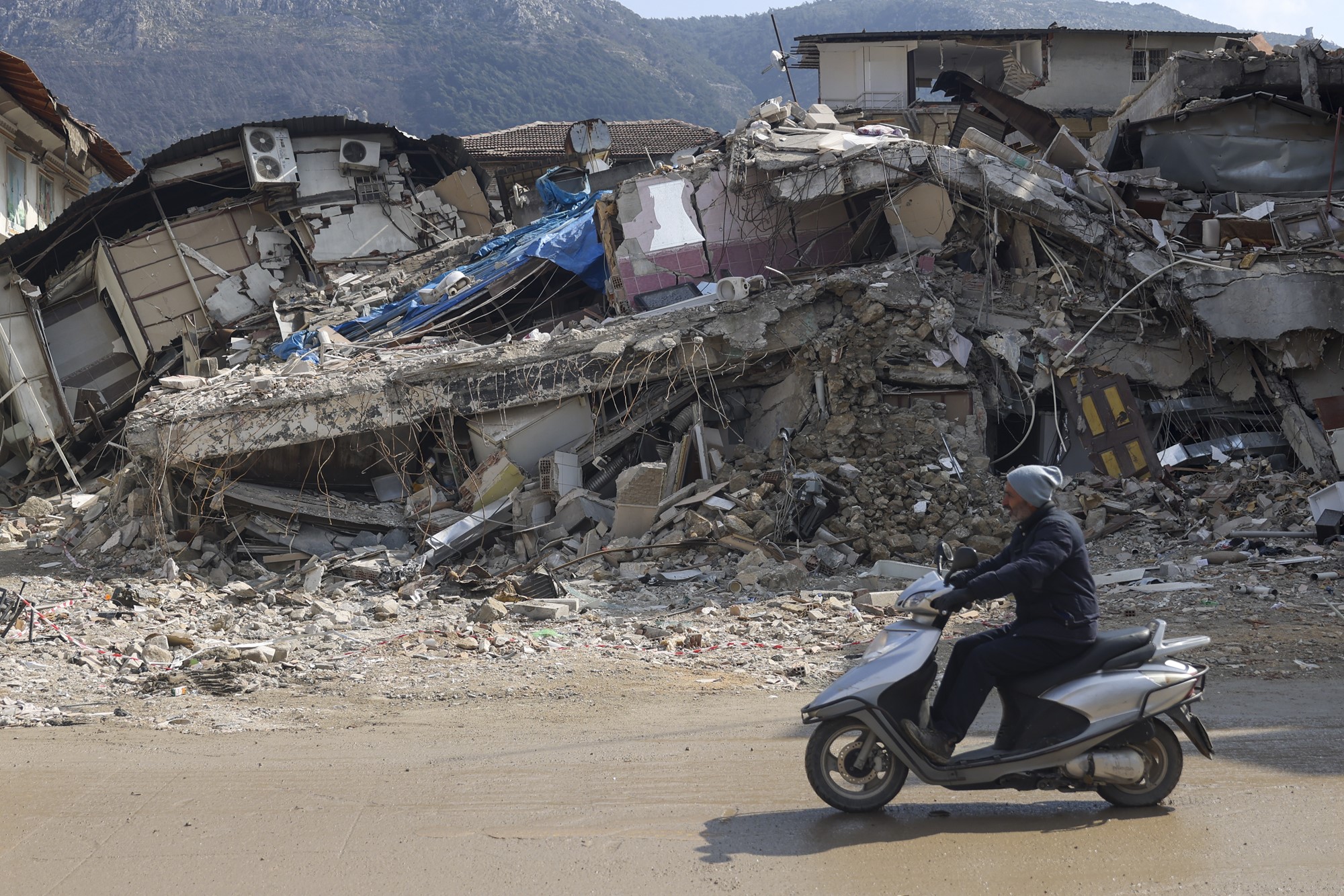 A man rides a moped past a destroyed building.