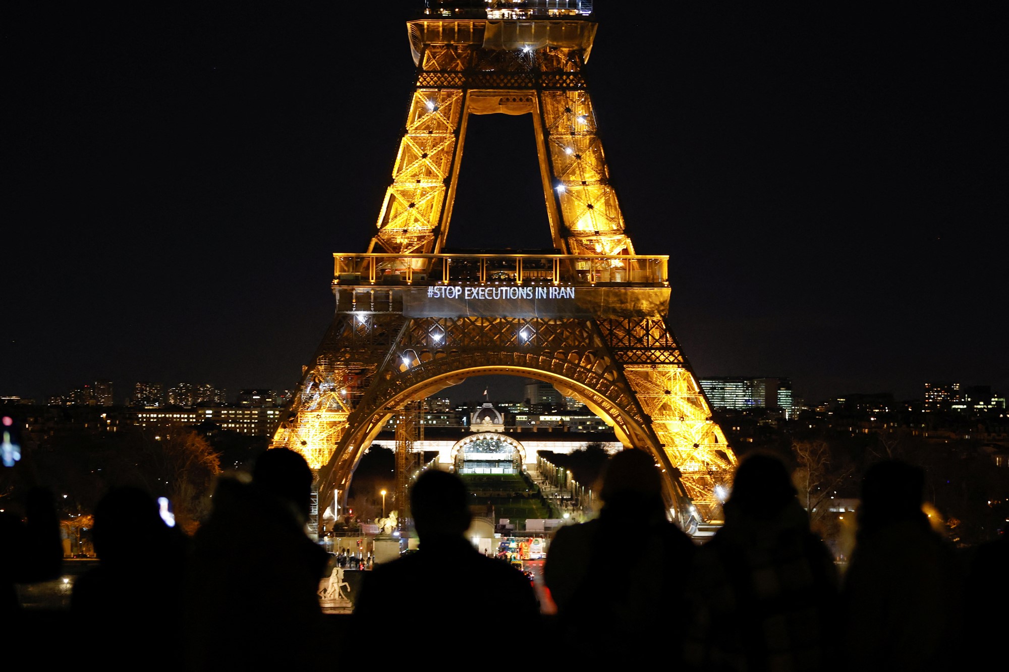 People take photos of the Eiffel Tower at night with the words #StopExecutionsInIran projected.