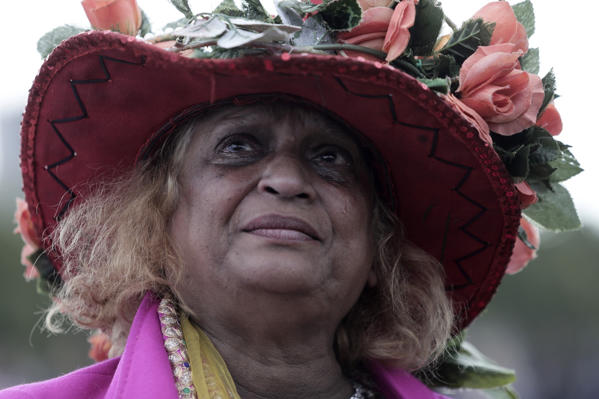 A lady wears a hat topped with flowers. She is crying