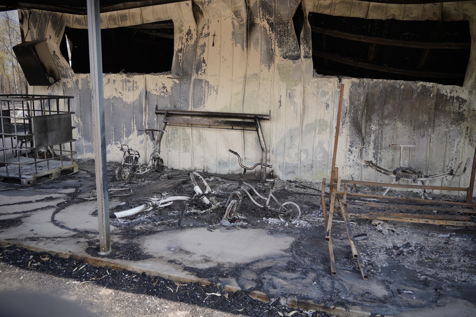 the burnt-out remains of a front porch of a home destroyed by a bushfire. kids bikes can be seen among the ashes