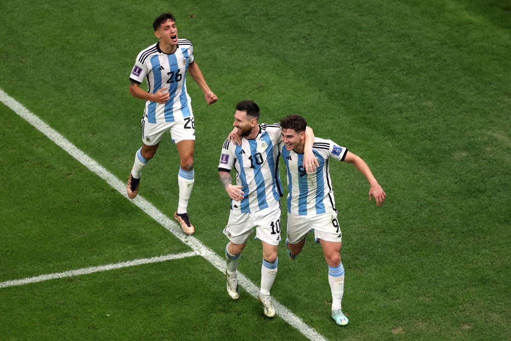 Lionel Messi puts his arm around Julian Alvarez as they celebrate a goal in the World Cup semifinal against Croatia. Nahuel Molina is running behind them.