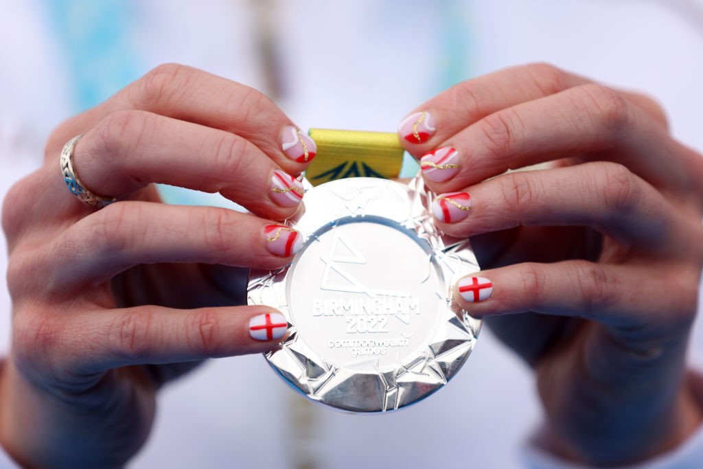 a close up of a woman holding a silver medal with red and white print nails
