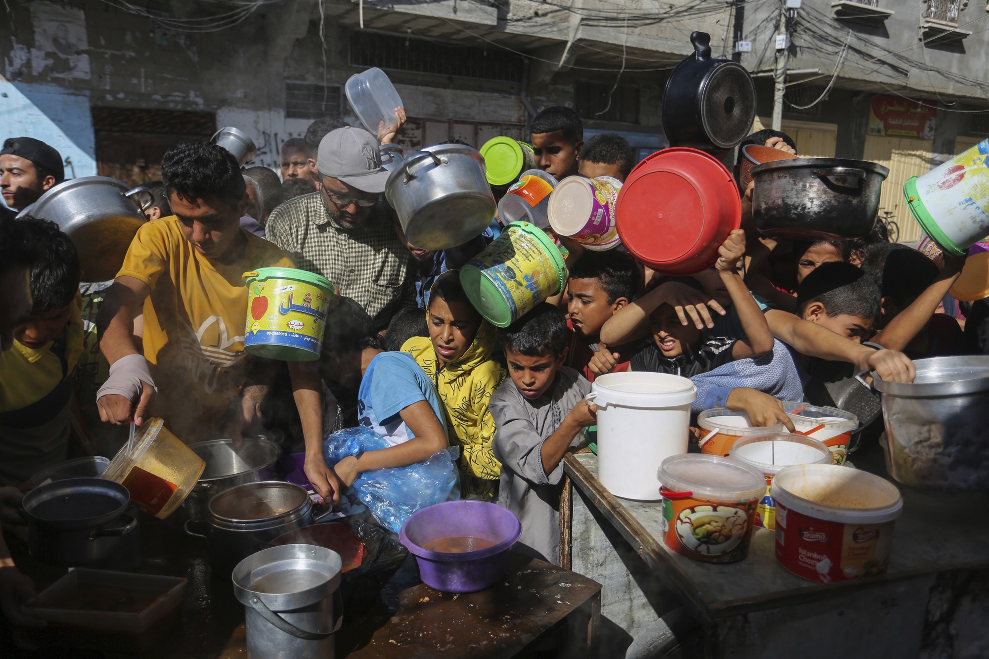 An image of people with pans and pots trying to get food from a distributor in Rafah, Gaza.