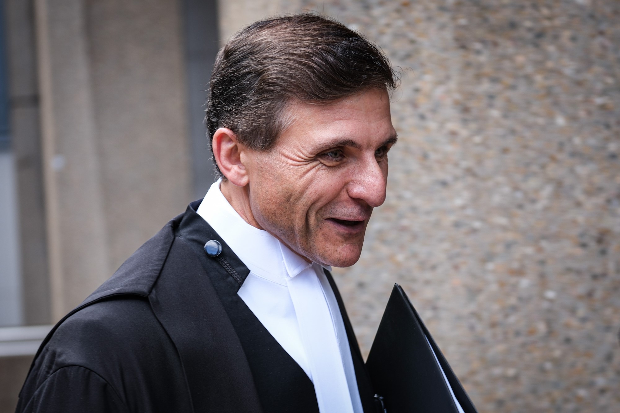 A man in black suit holding folder smiling
