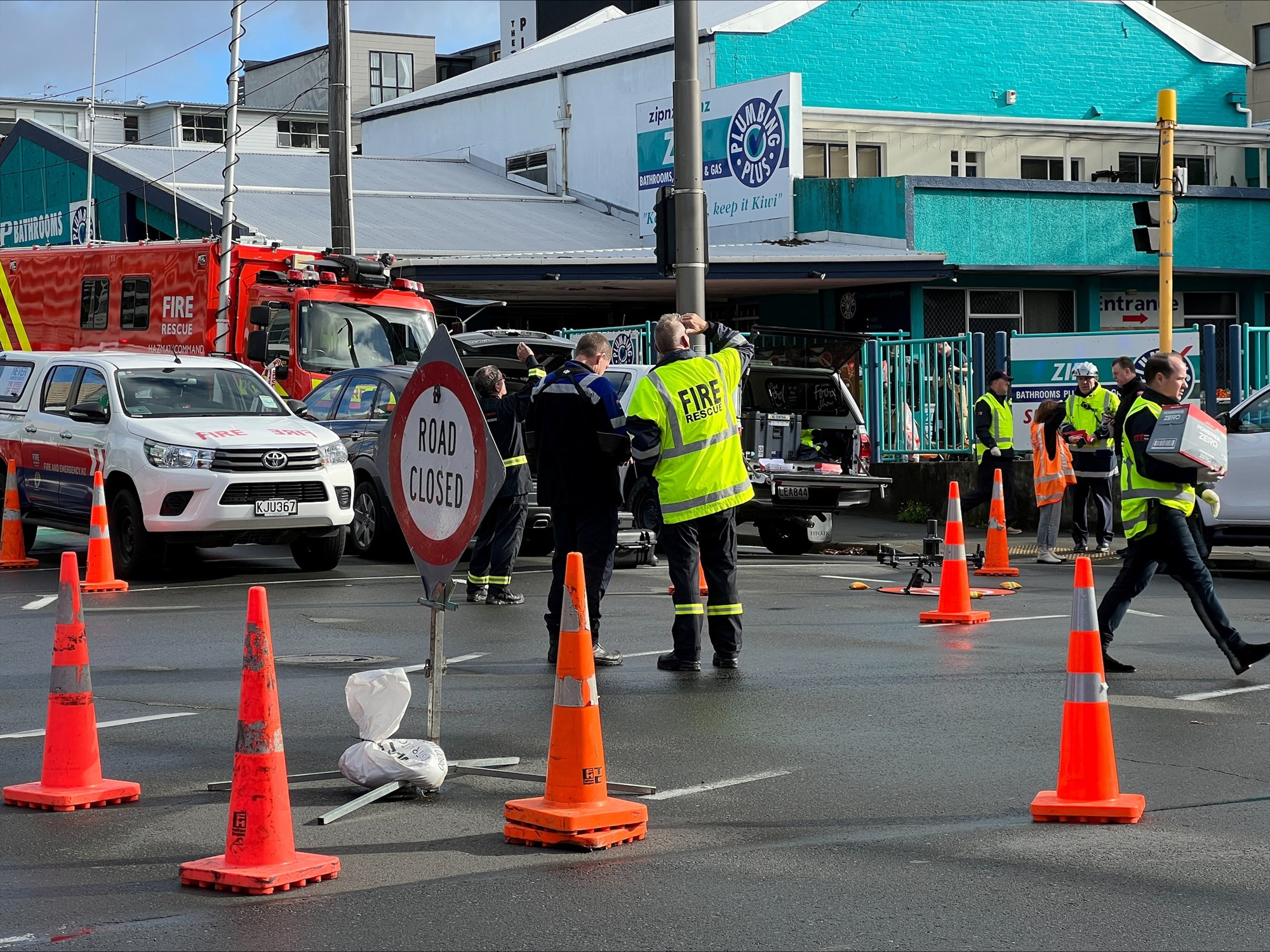 Fire and rescue crews stand on a blocked road and look at a building.