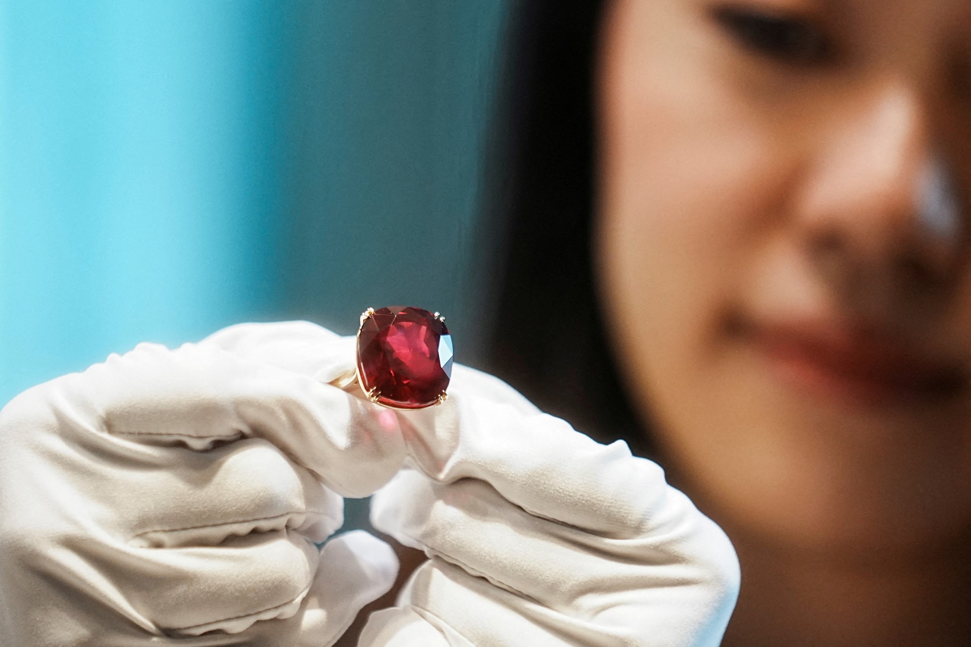 An Asian woman with white gloves holds a red ruby ring
