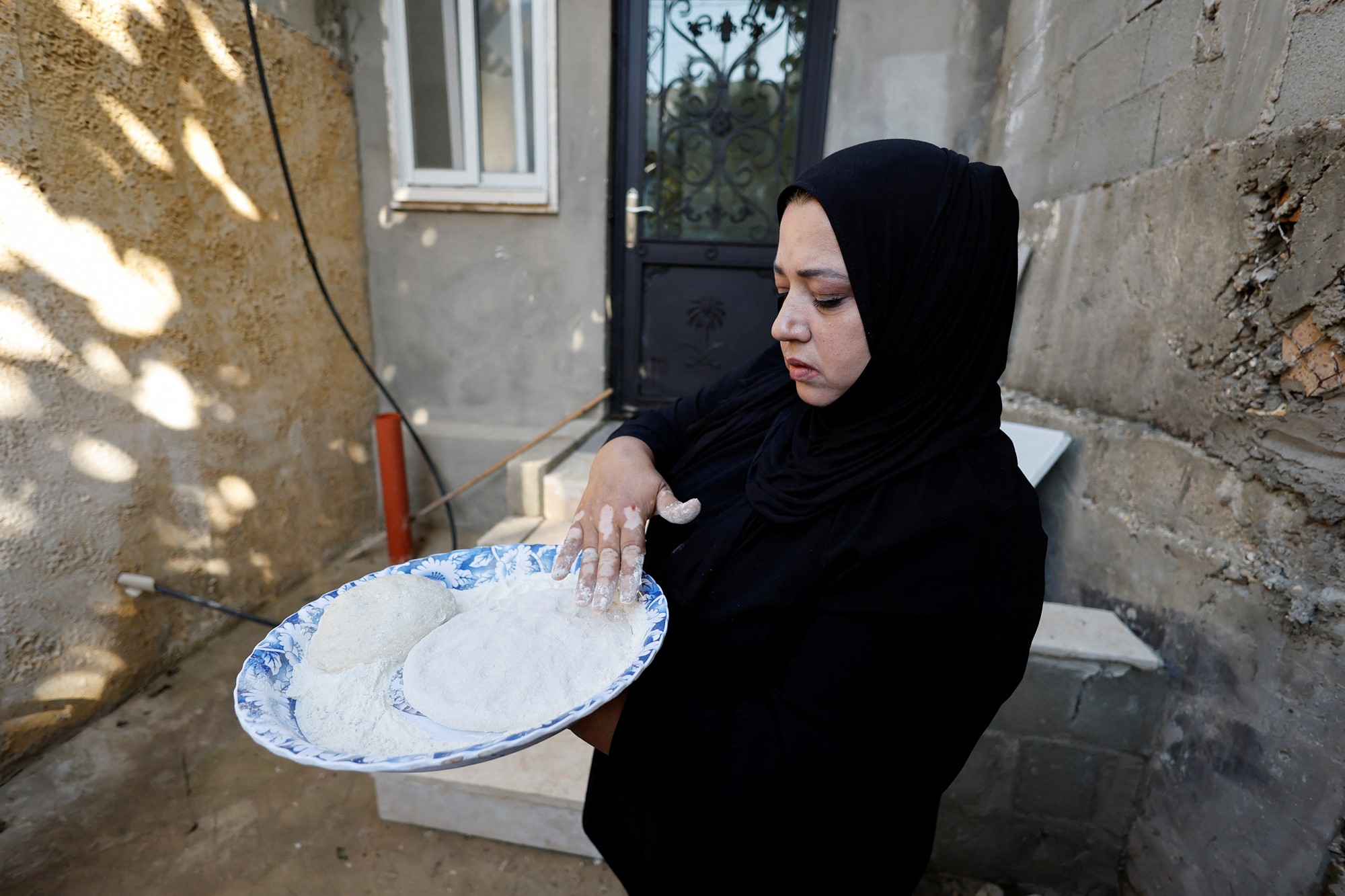 a woman wearing black holding a blue plate with dough on top of it