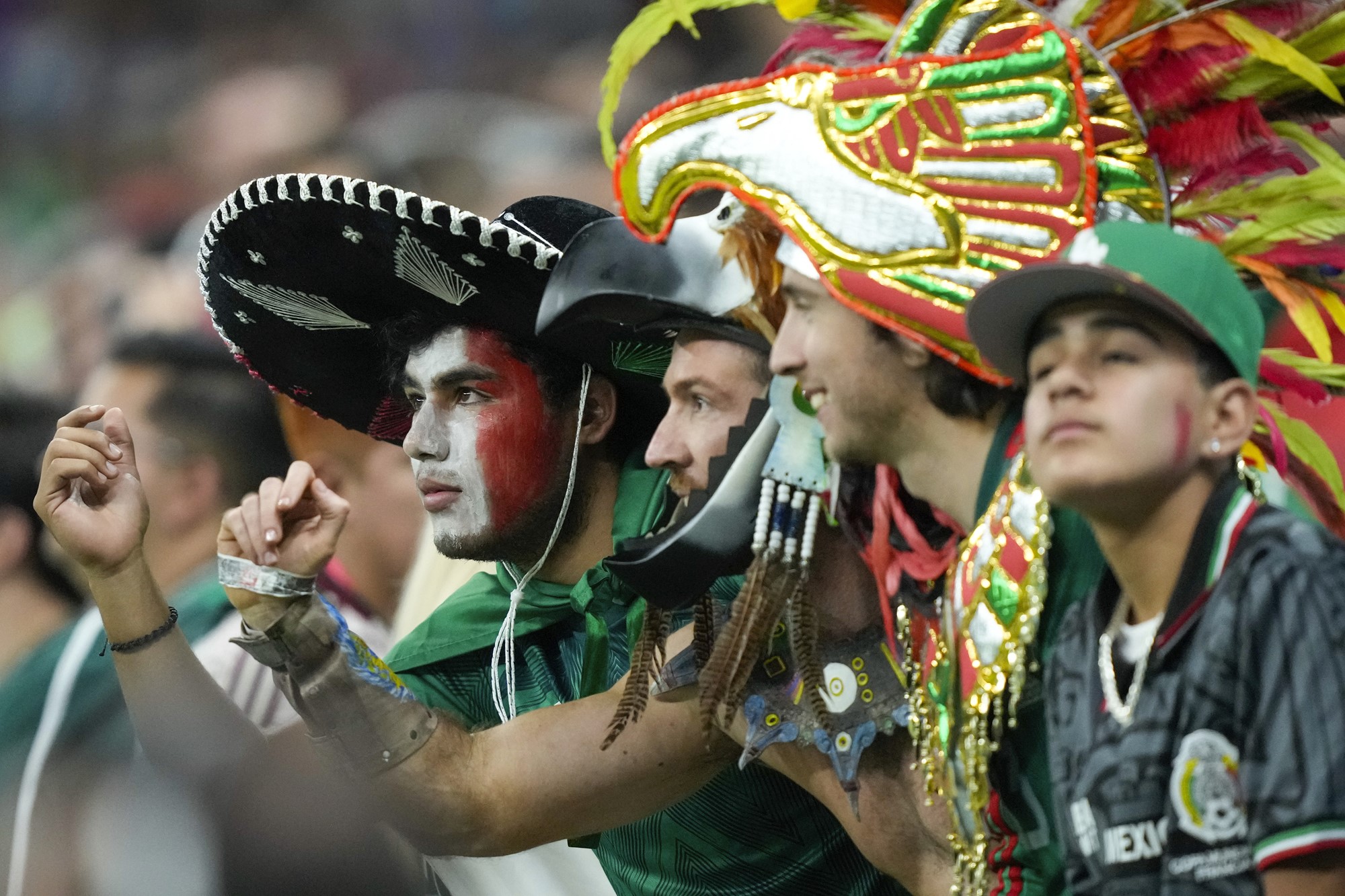 A group of Mexican football fans wearing hats and colourful gear stare at the action on the pitch during a World Cup match.