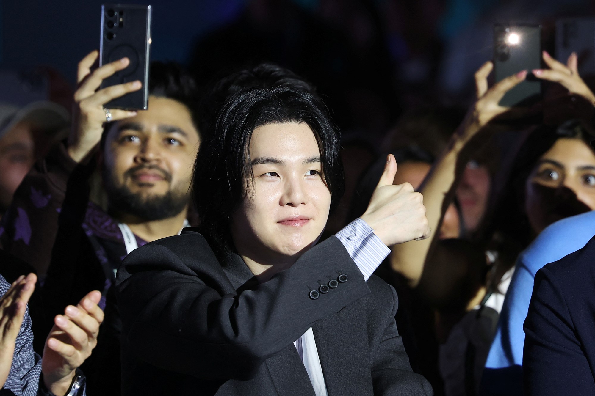 K-pop star Suga gives a thumbs up in a suit.