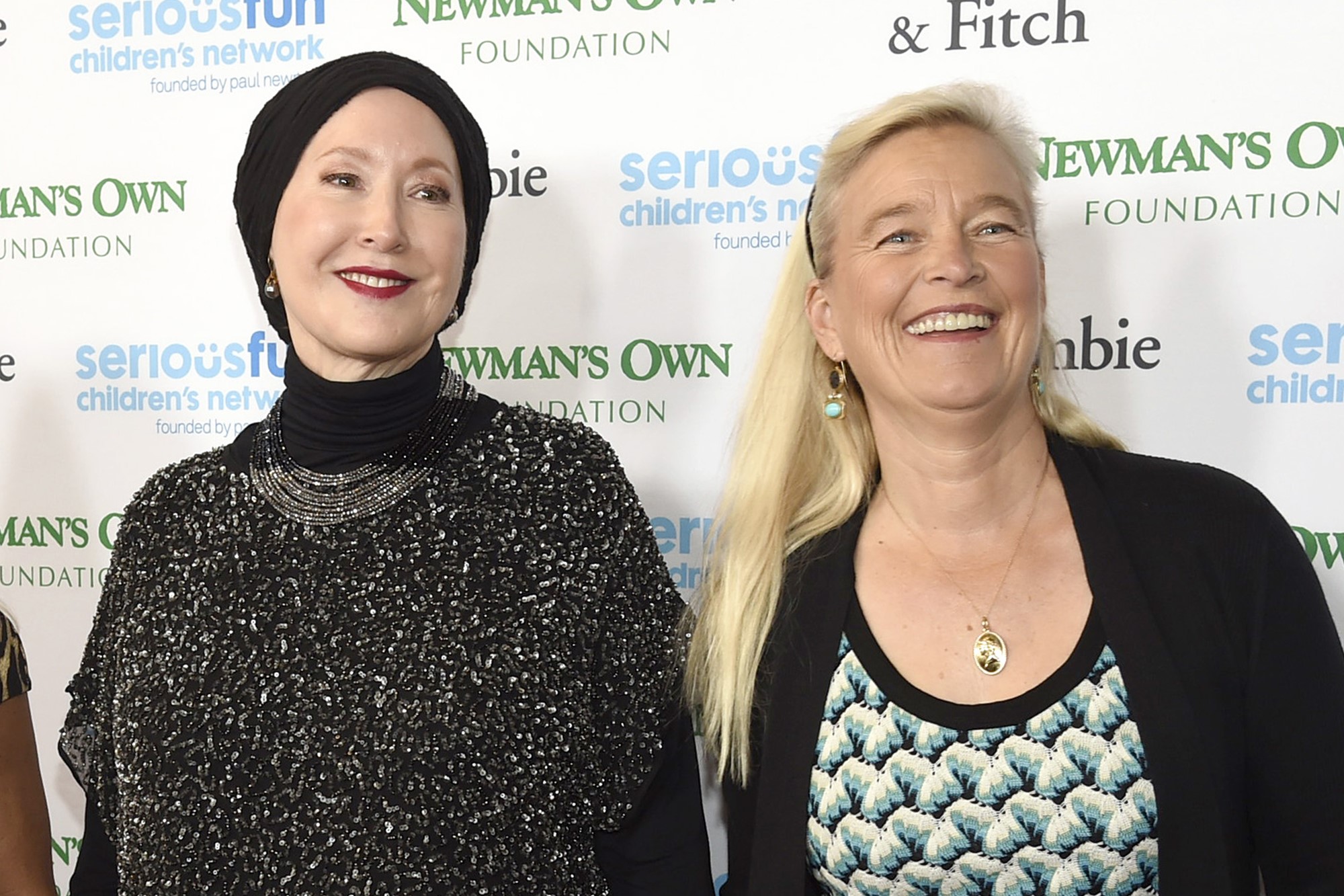 Two white women, Susan Newman and Nell Newman, stand and smile in front of a promotional banner at a media event.