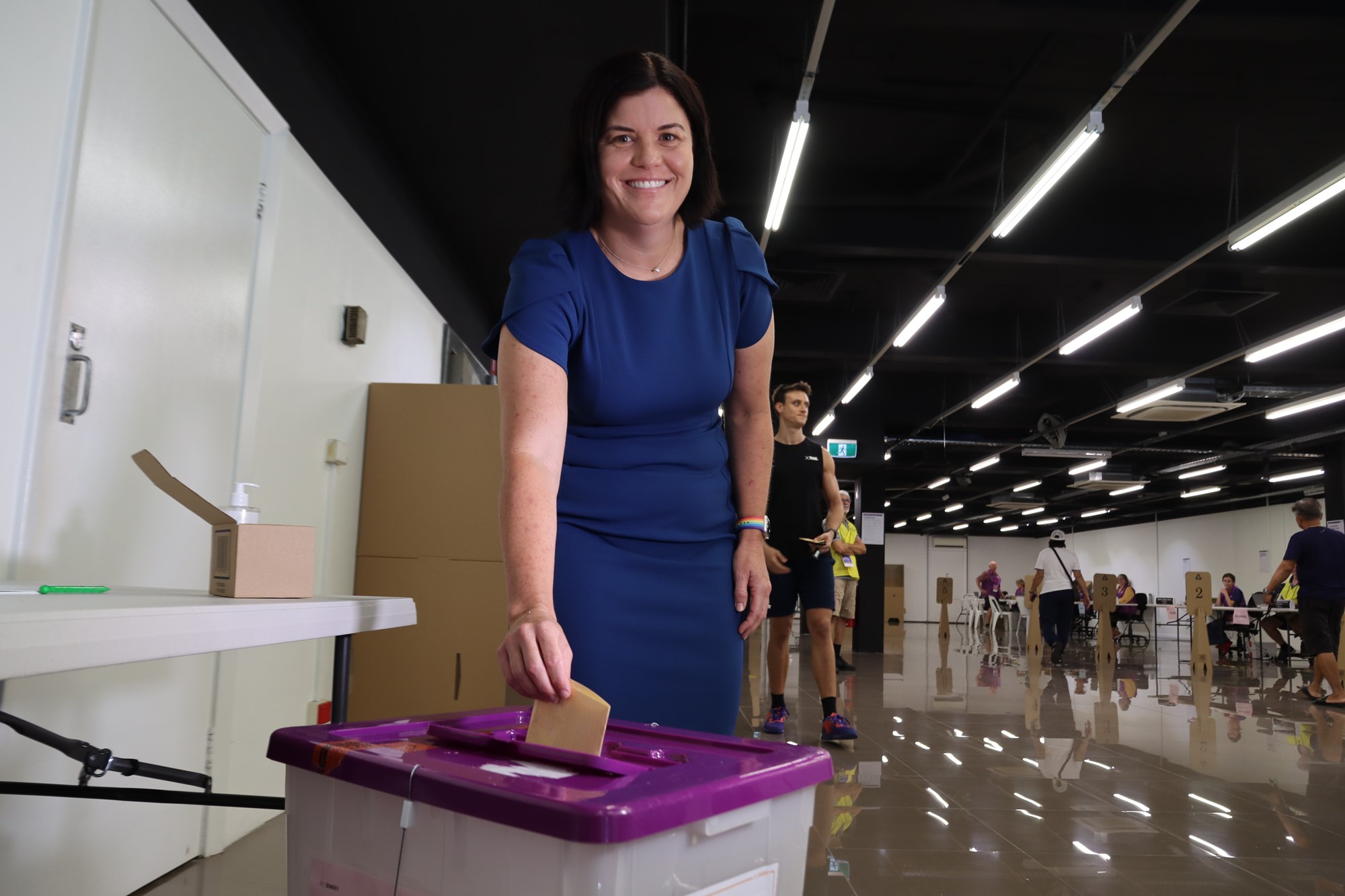 Natasha Fyles in a blue dress places a ballot in a box at a voting centre while smiling at the camera