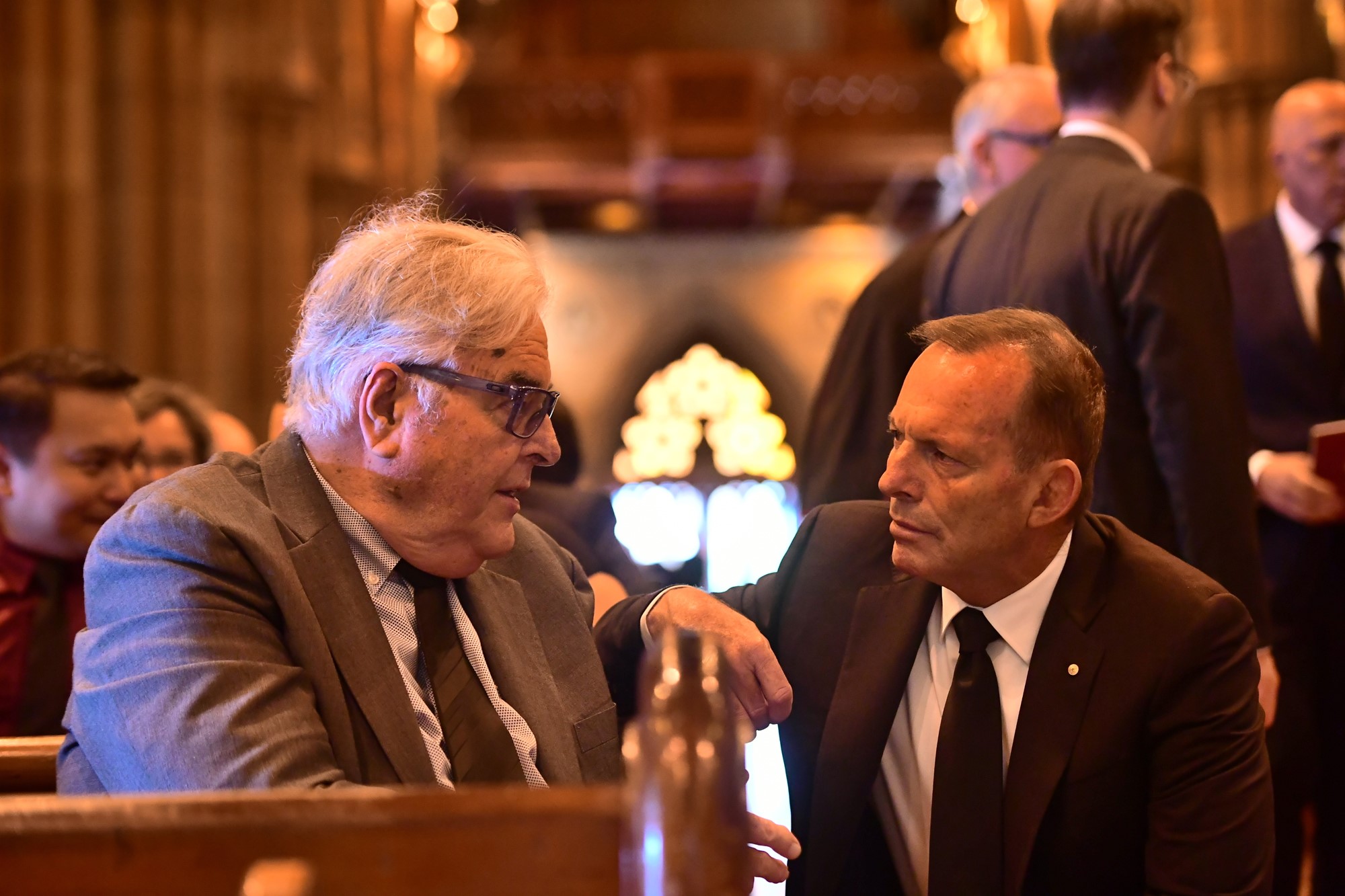 David Pell sits on a pew talking to Tony Abbott.