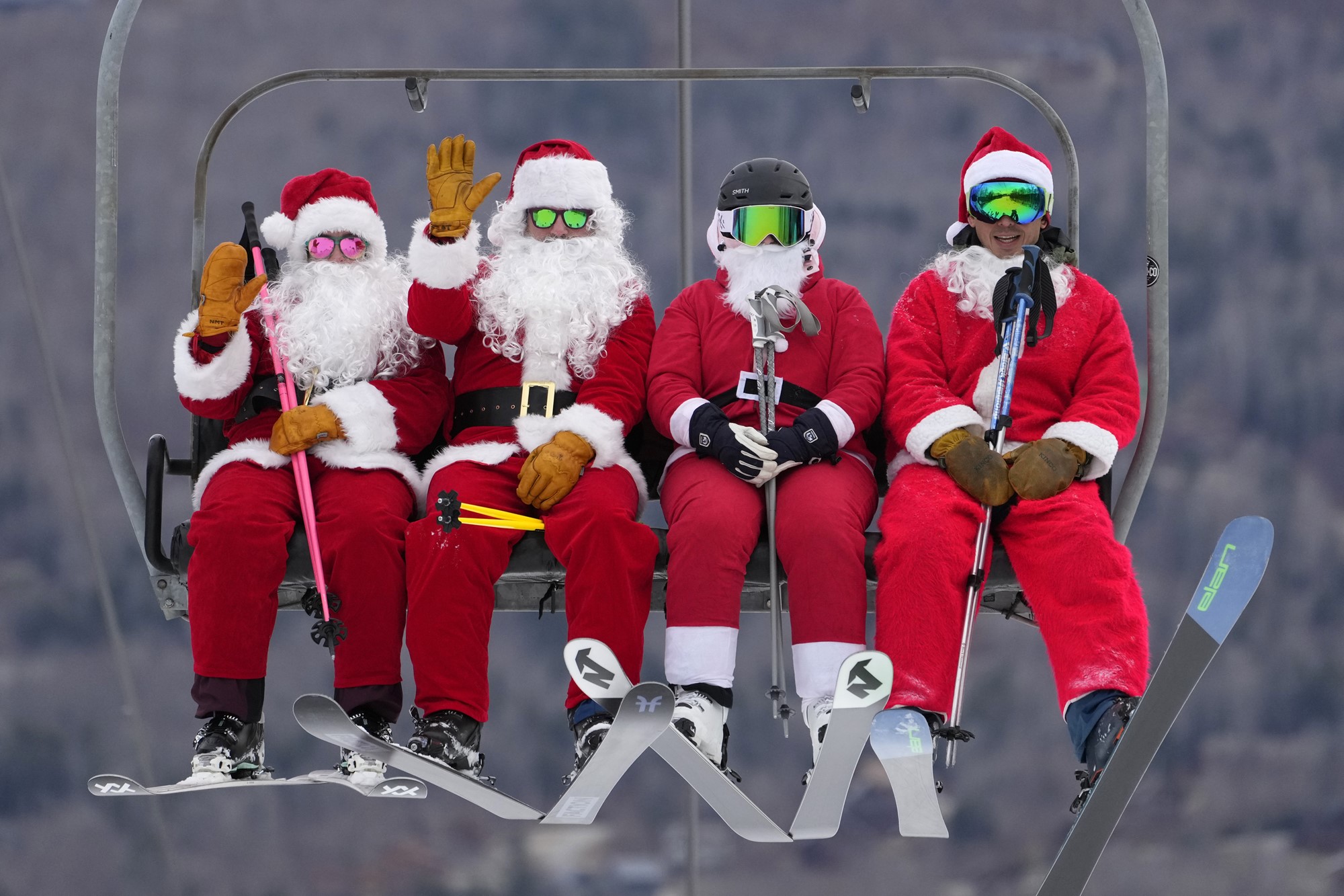Four people in ski gear and santa costumes sit on a ski lift. 