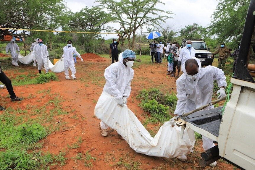 Forensic workers retreive a body wrapped in white material.