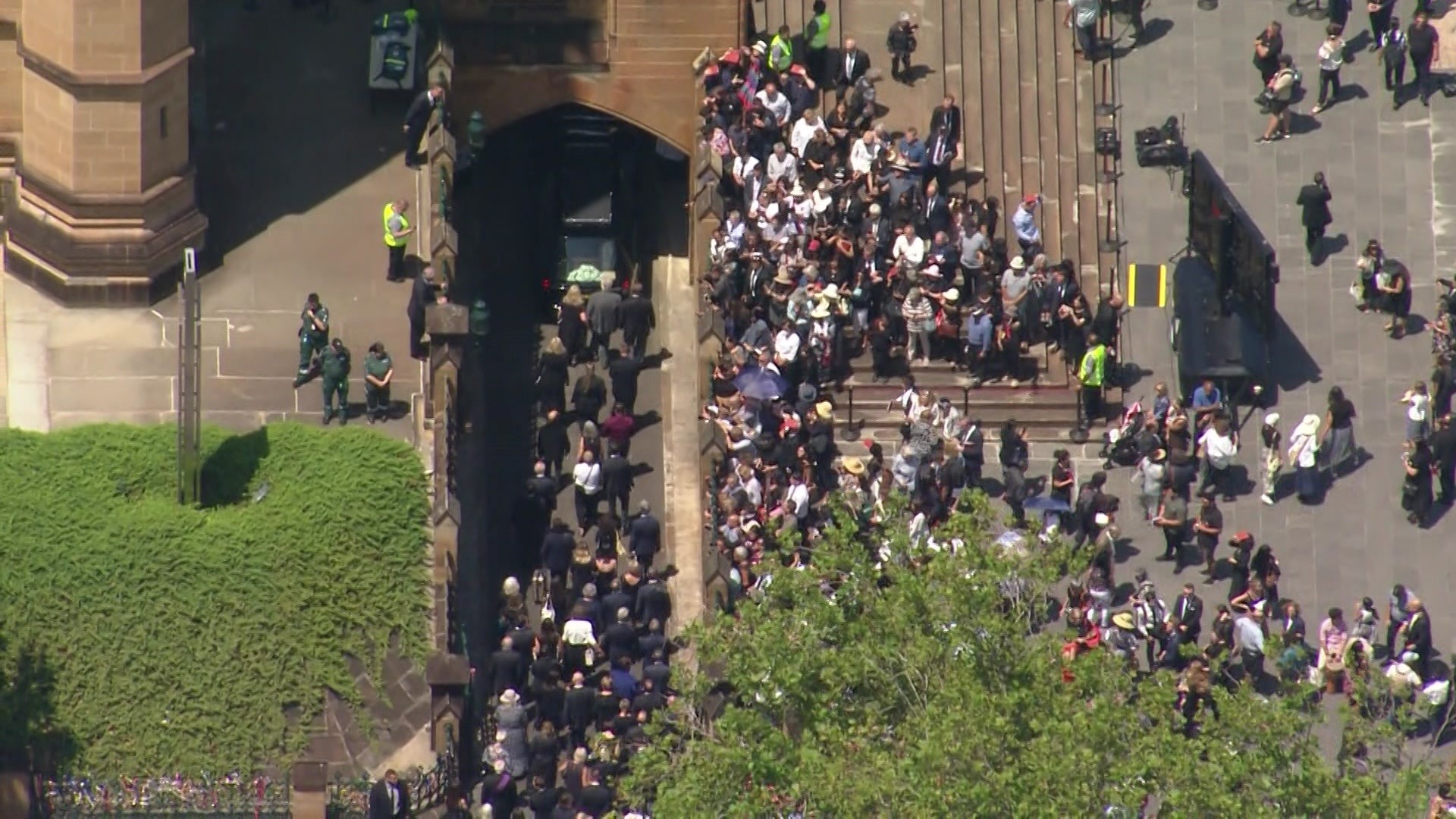 Aerial view of people walking behind a hearse