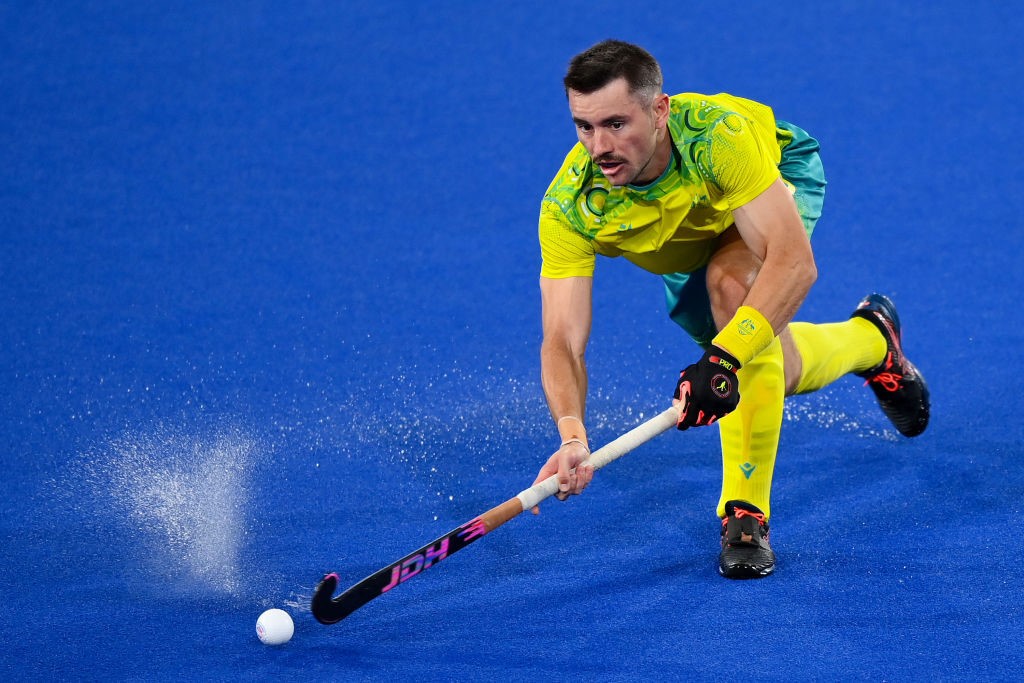 A hockey player drags his stick towards the ball with spray coming up behind it
