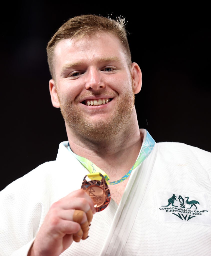 a judo athlete wearing a top with the australian crest holds a bronze medal and smiles