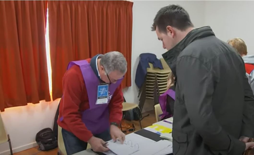 A man getting details checked by a volunteer at a voting centre