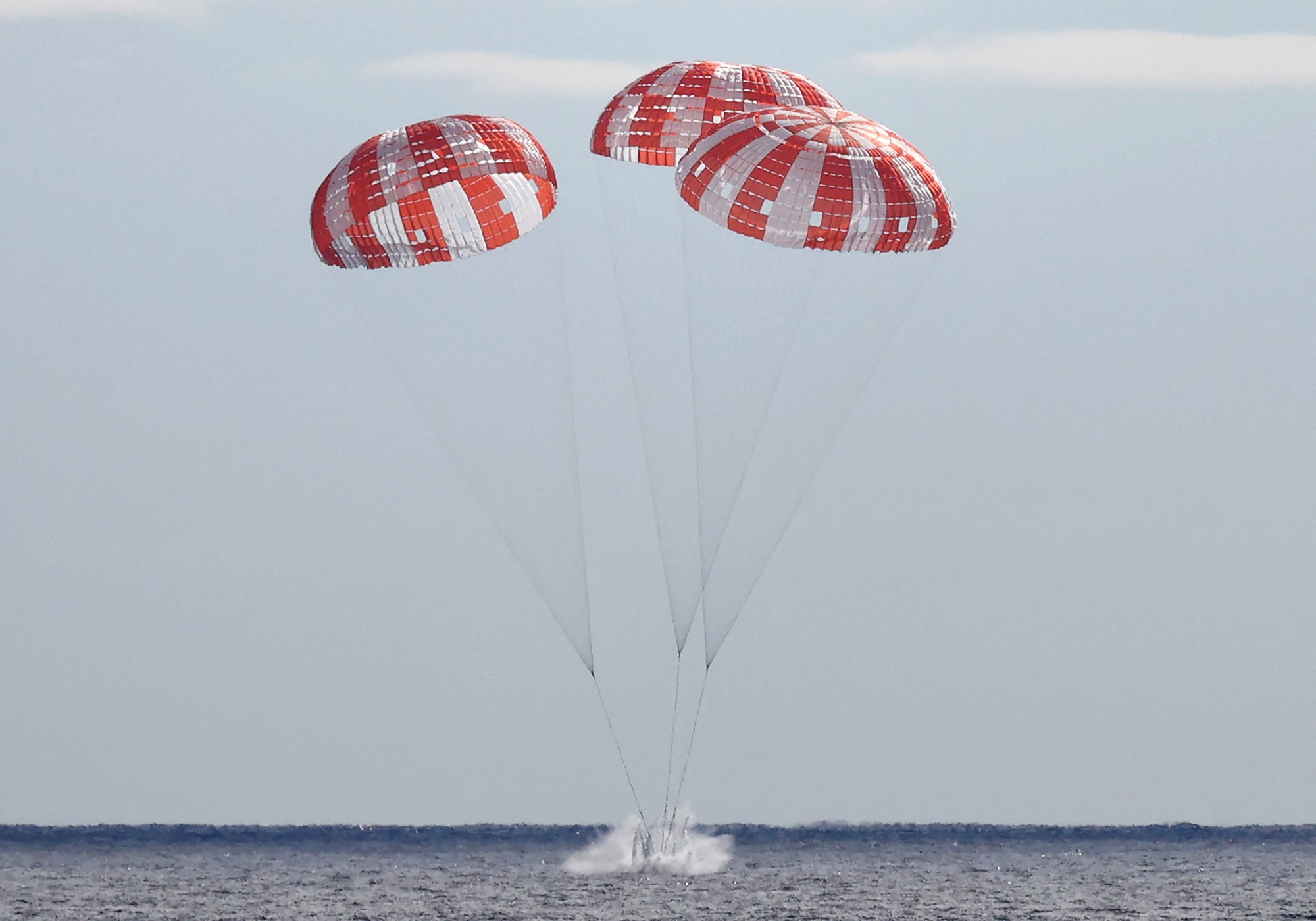 The Orion capsule splashes into the ocean with three large parachutes hanging off it. 