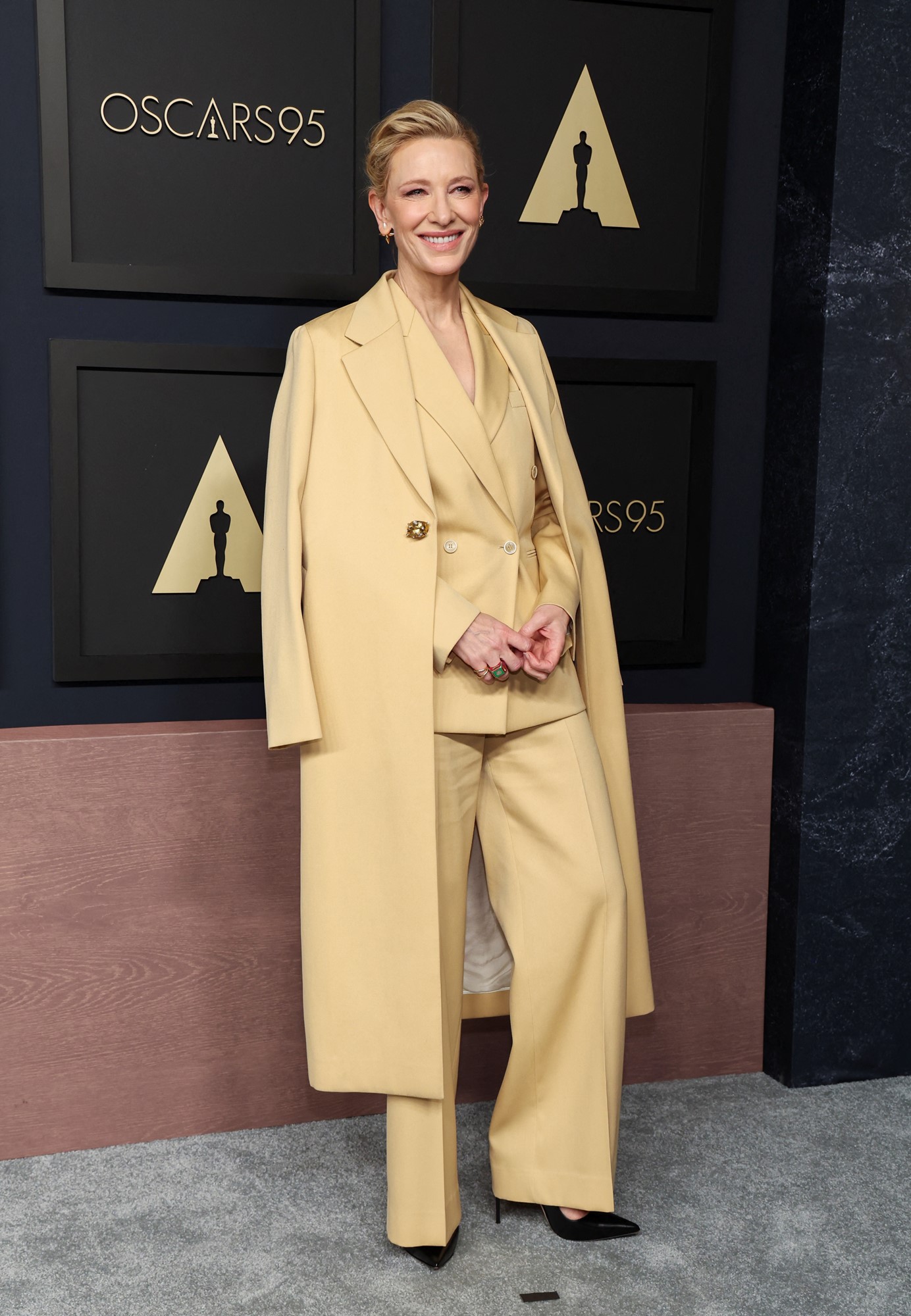 Cate smiles in a yellowy beige oversized suit.