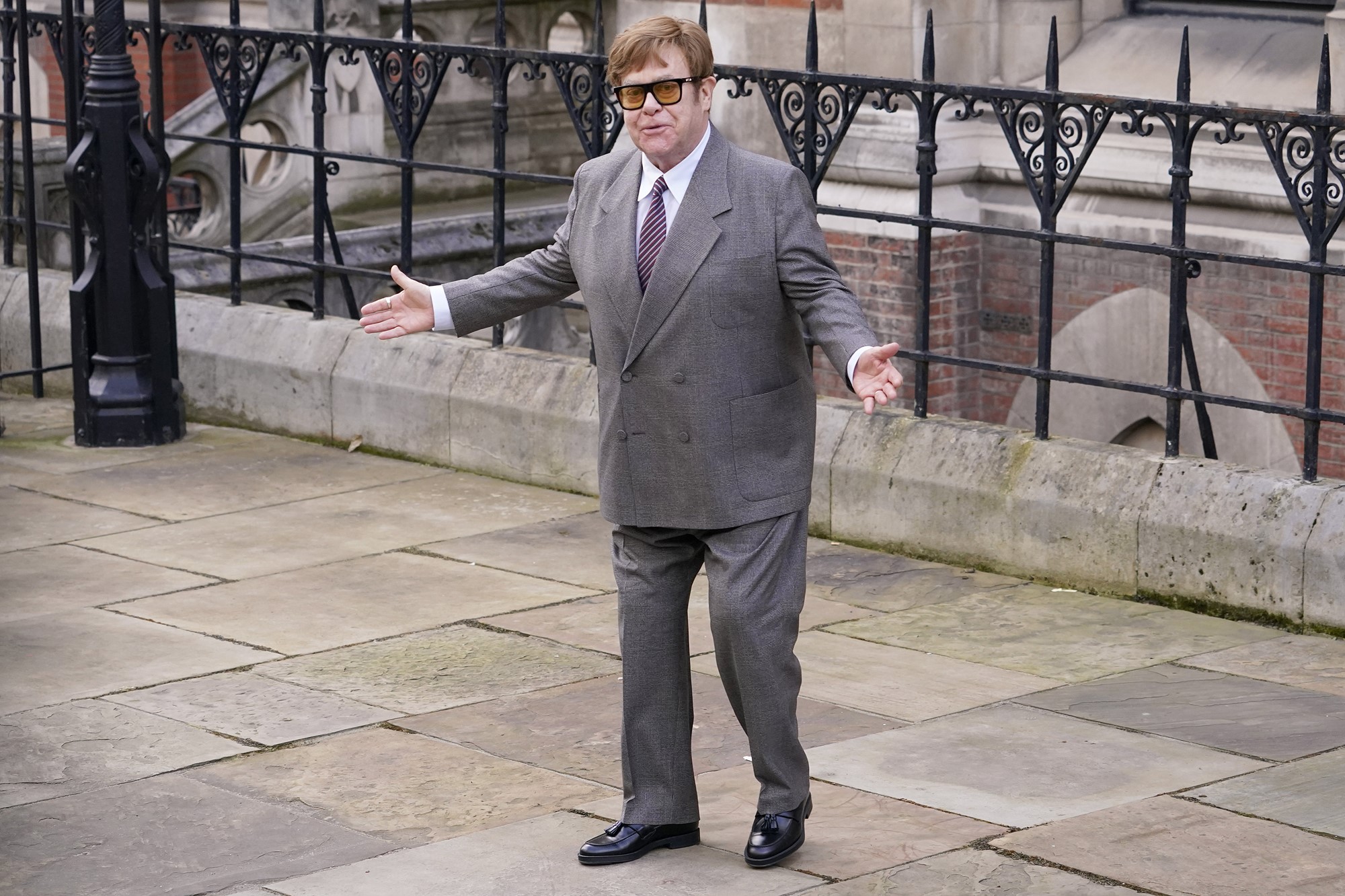 Elton John on a street in a suit.