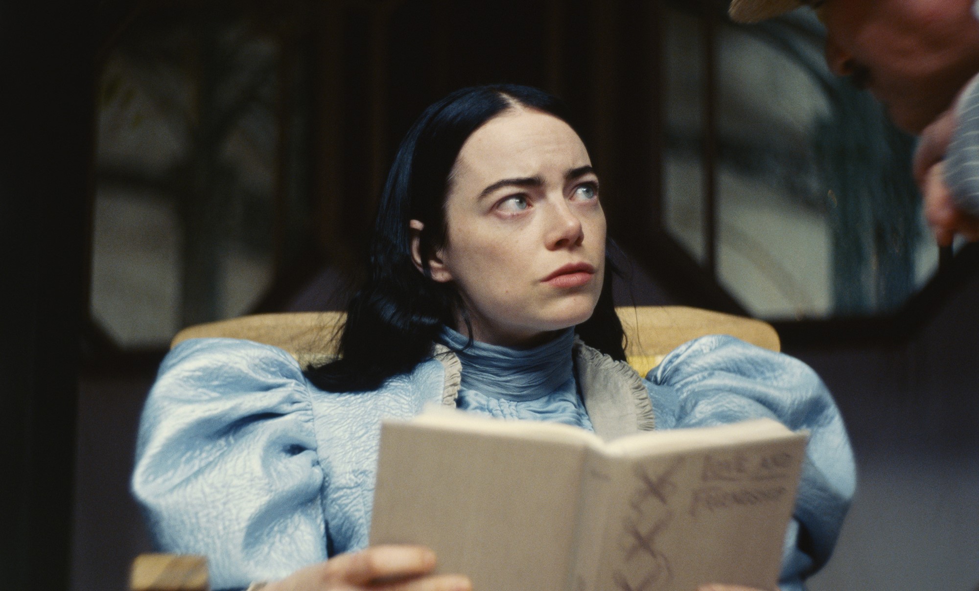 Emma Stone reading a book in Poor Things. 