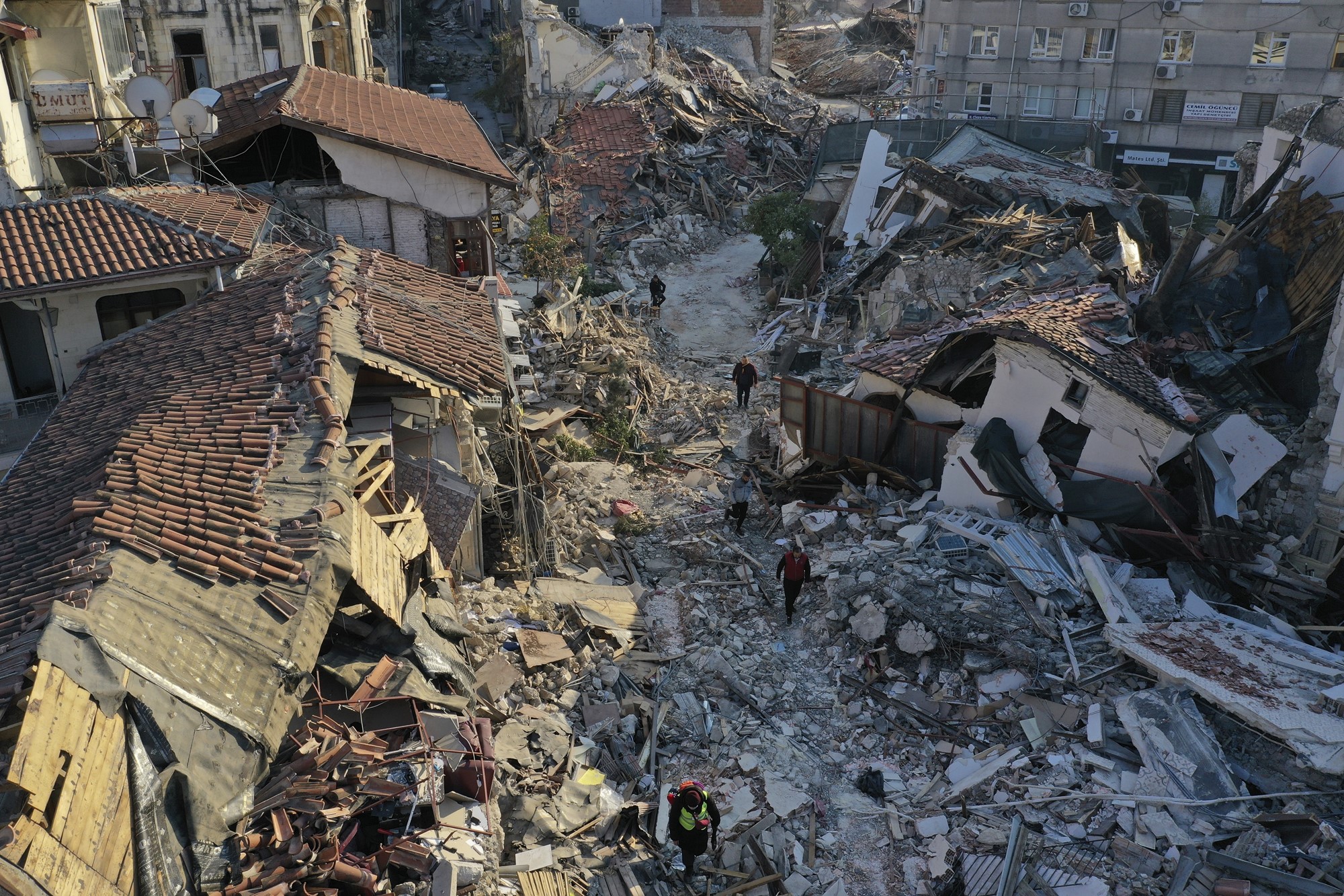 A city street is turned to rubble as people walk past crumbled buildings. 