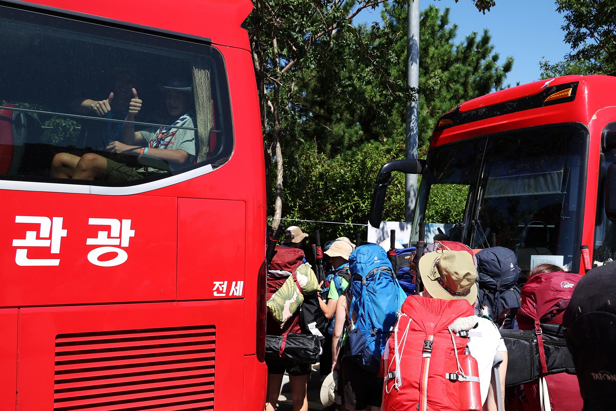 Participants sitting inside a bus give a thumbs-up as they prepare to leave the camping site of the 25th World Scout Jamboree in Buan, South Korea