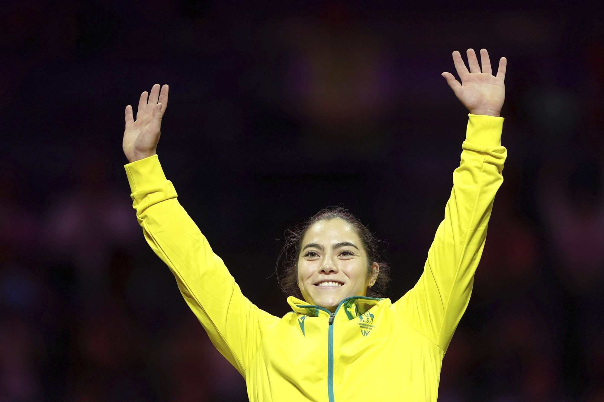 gymnast georgia godwin smiles and waves both arms in the air wearing a yellow australia branded jacket