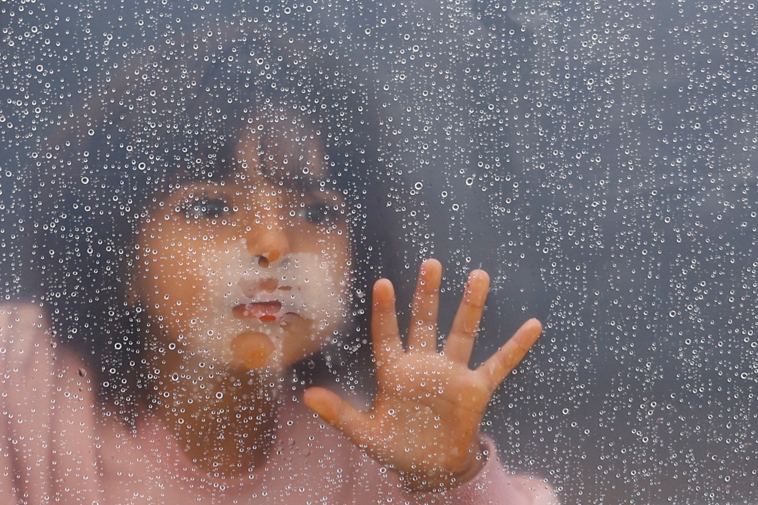A little girl looks through a window in a  refugee camp 