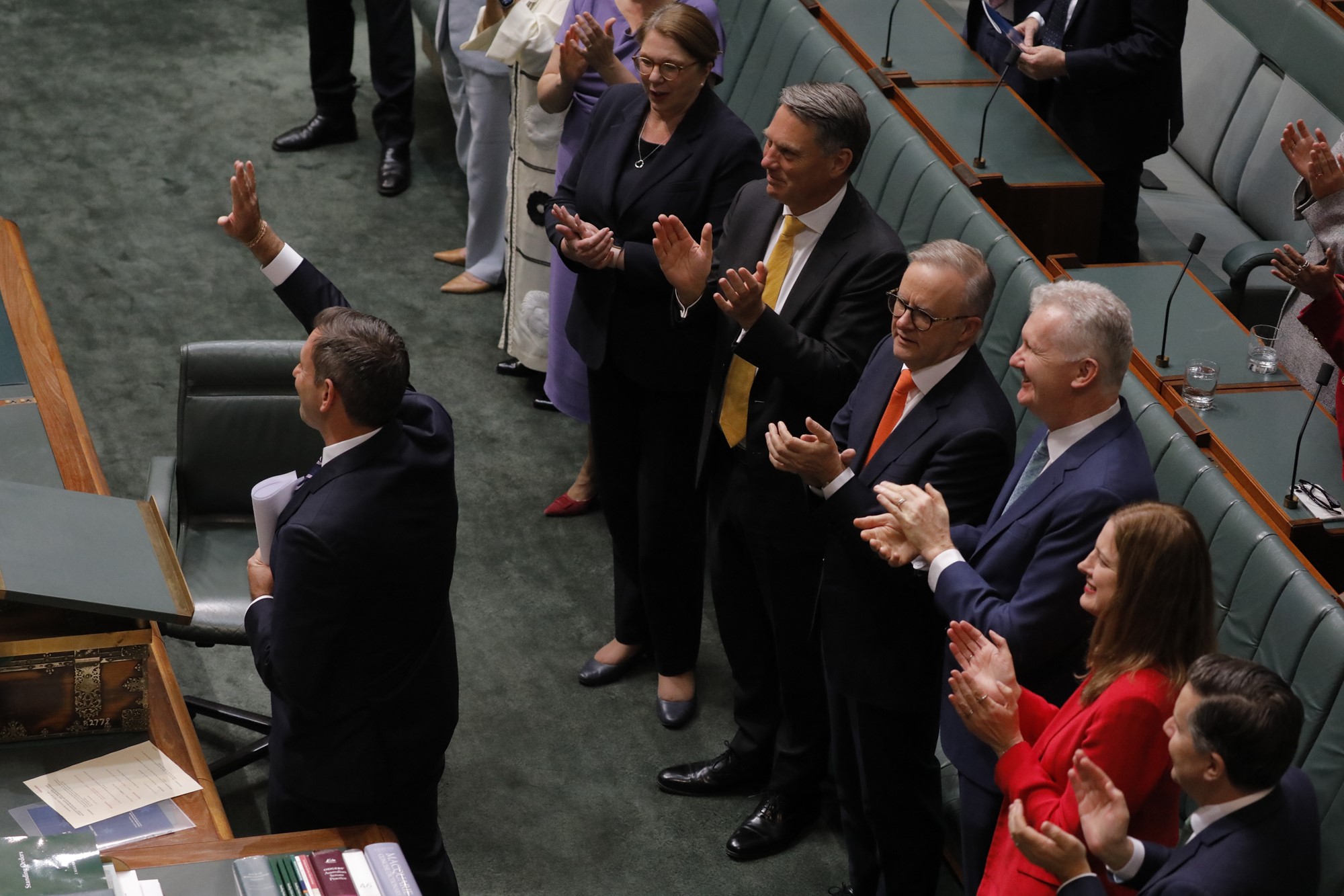 The Treasurer stands in Parlaiment waving as people applaud him following the budget speech.
