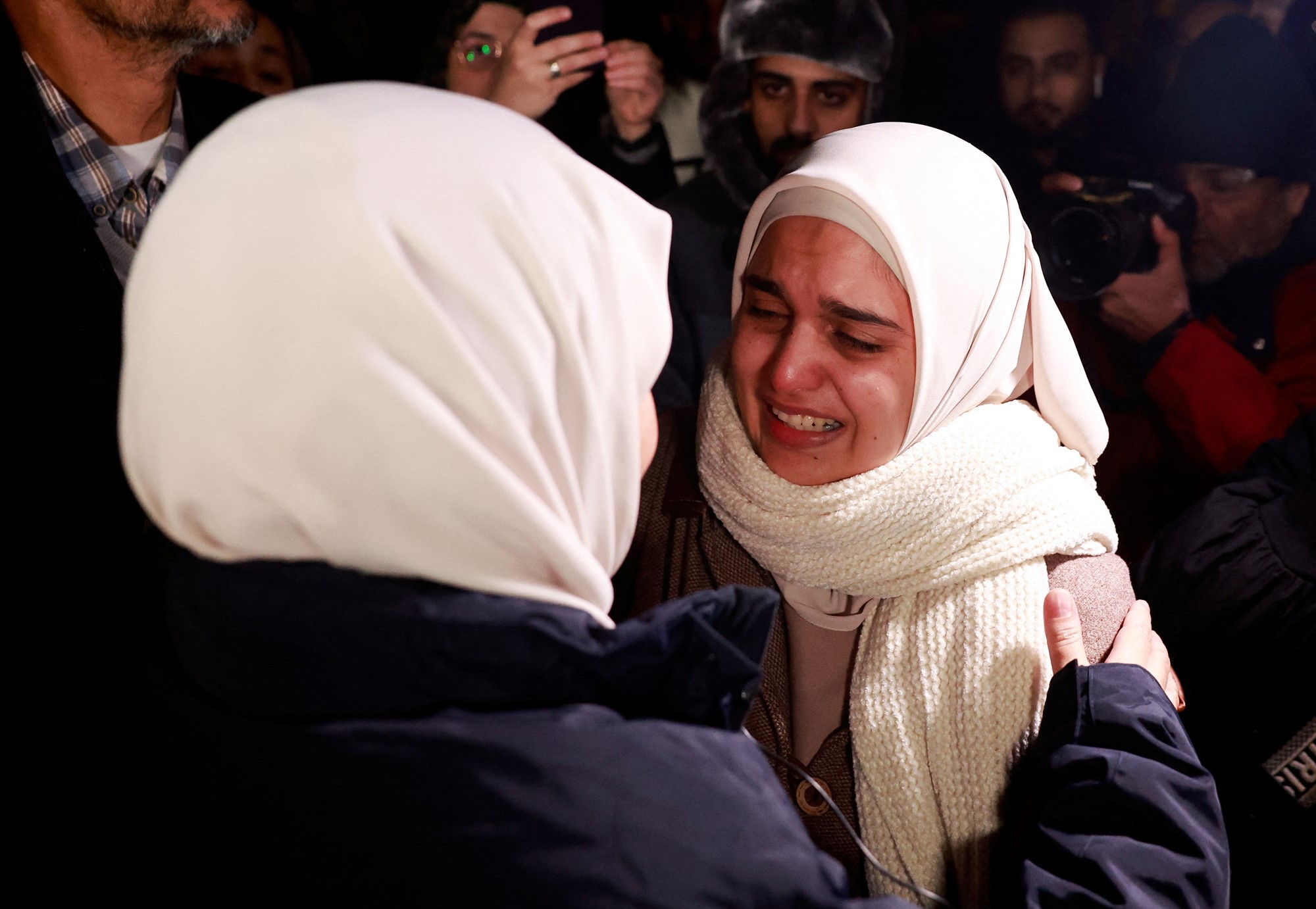 A close up of two women wearing headscarves embracing, one crying