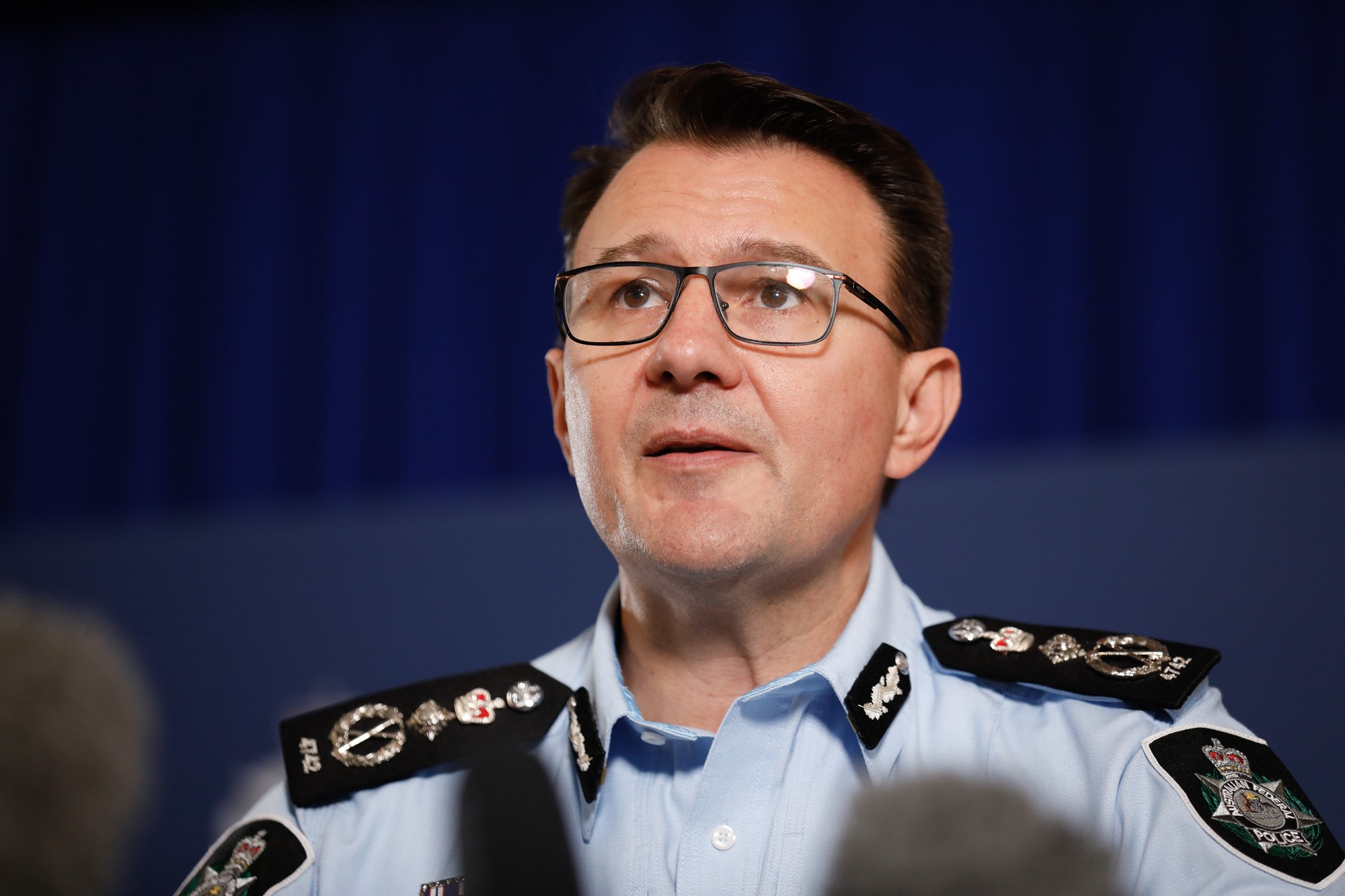 A man in an AFP uniform and glasses stands behind a podium addressing the media