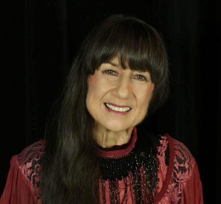 Judith Durham smiles, dressed in a red dress for a portrait photograph.