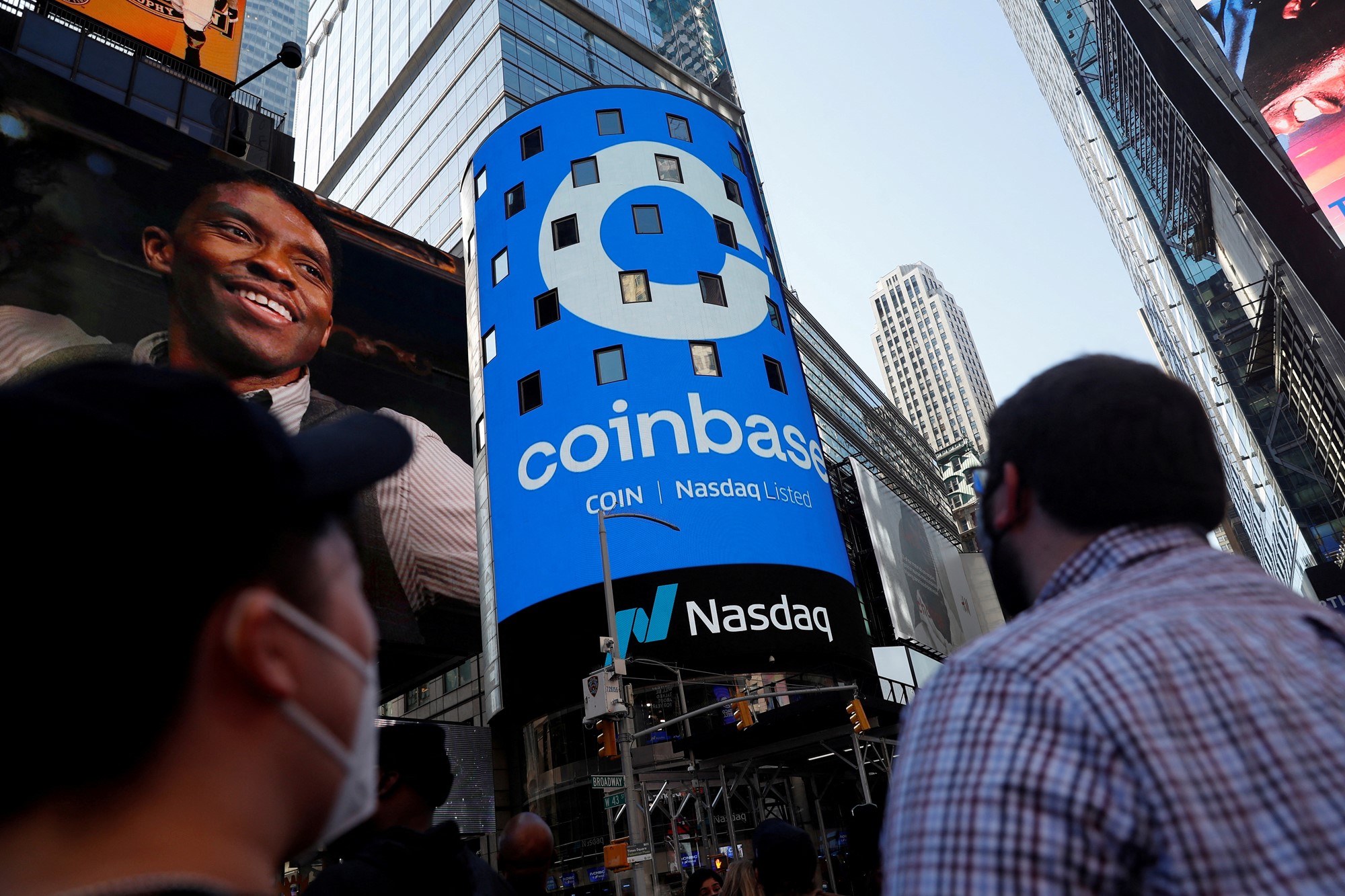 People look up at a blue advertisement for Coinbase on the side of a building at Times Square in New York.