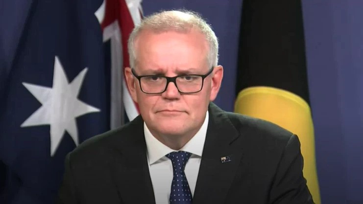 Scott Morrison stands in a suit in front of an Australian flag and Aboriginal flag