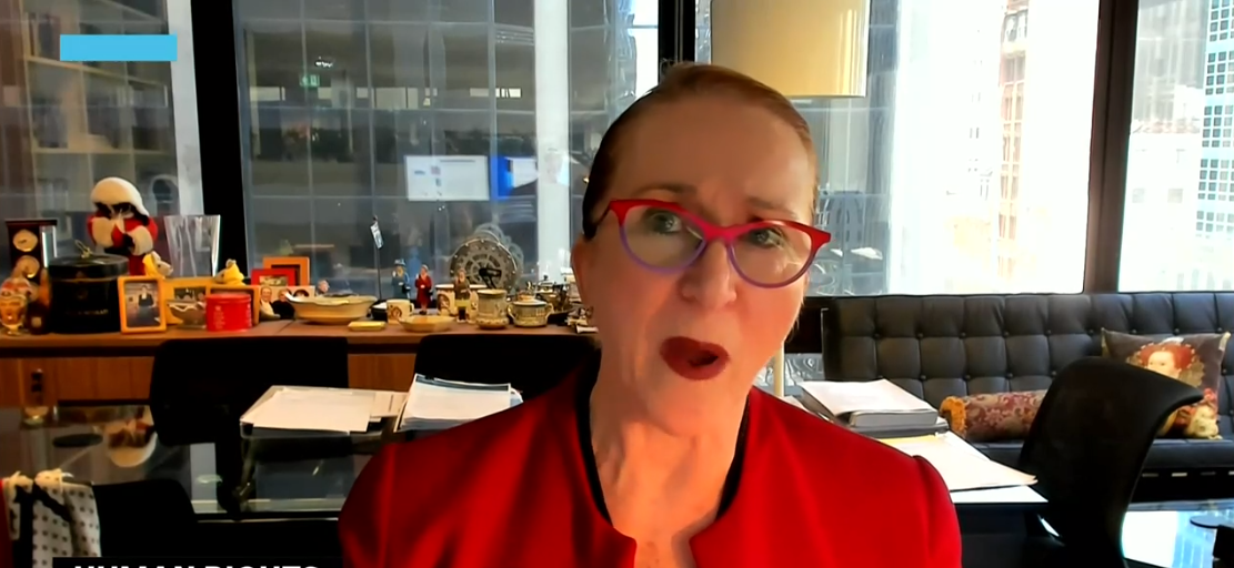 Woman wearing red glasses, shirt and lipstick sits in an office.