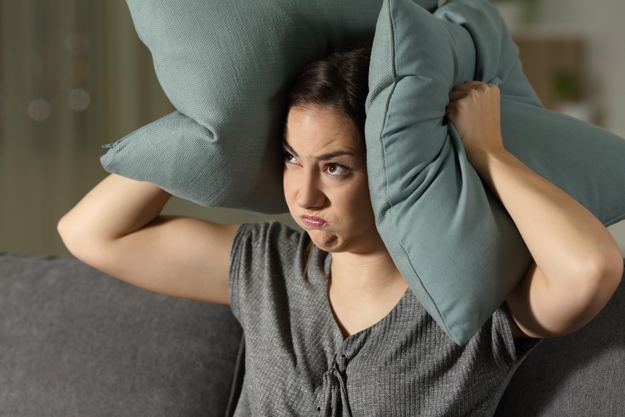 A woman holds a pillow over her ears