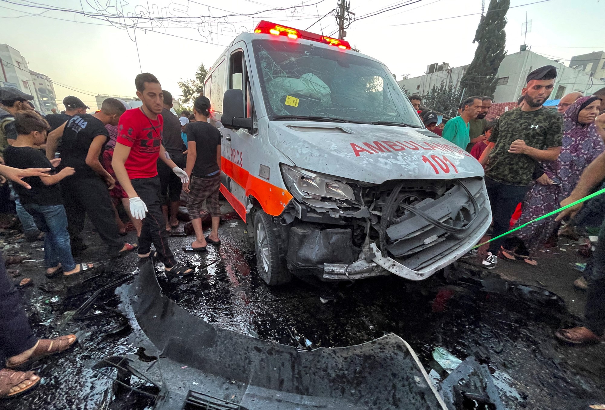 Young Palestinian men gather around a wrecked ambulance.