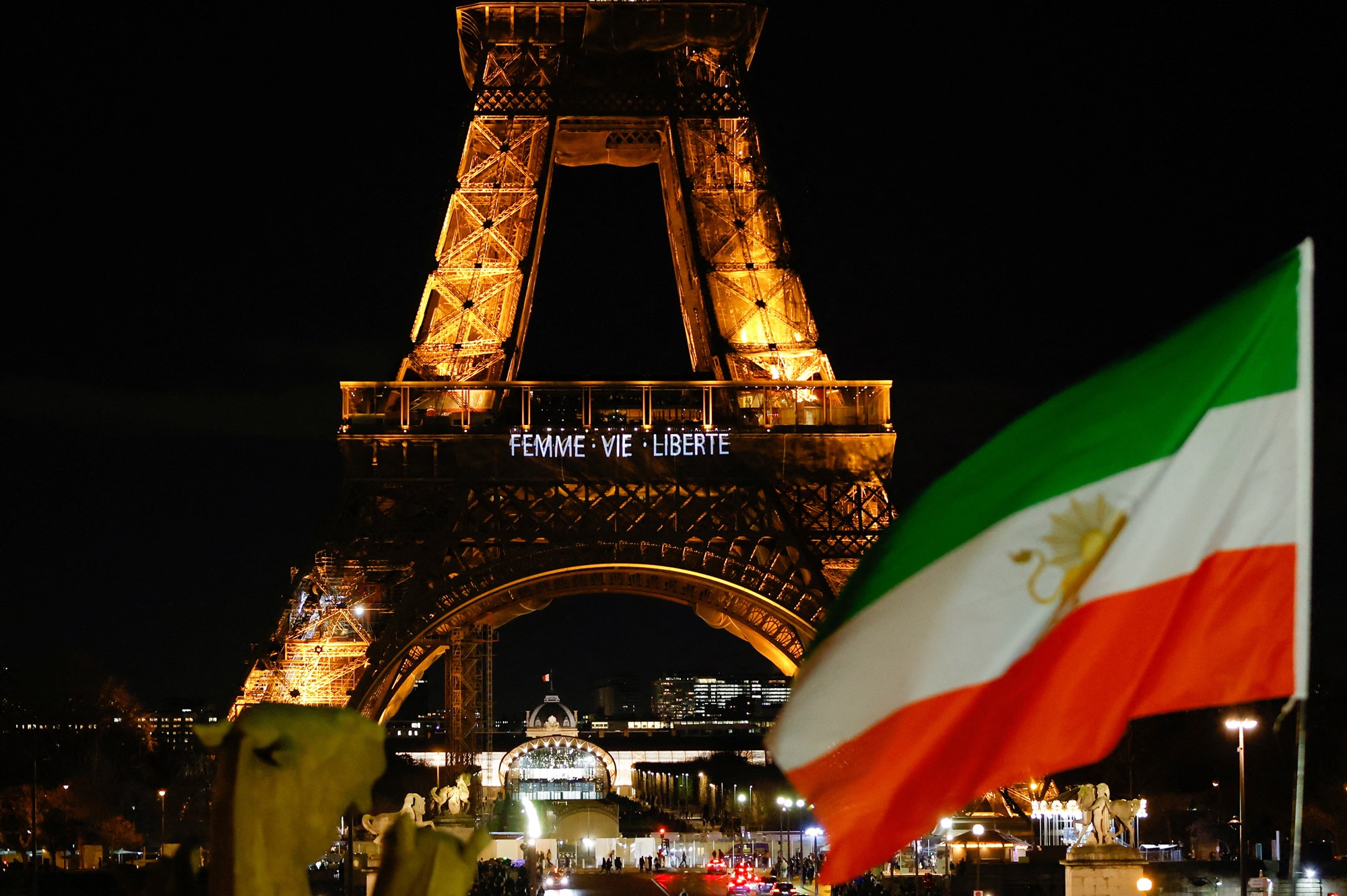 An Iran flag flies in front of the Eiffel Tower at night which reads "woman, life, freedom".
