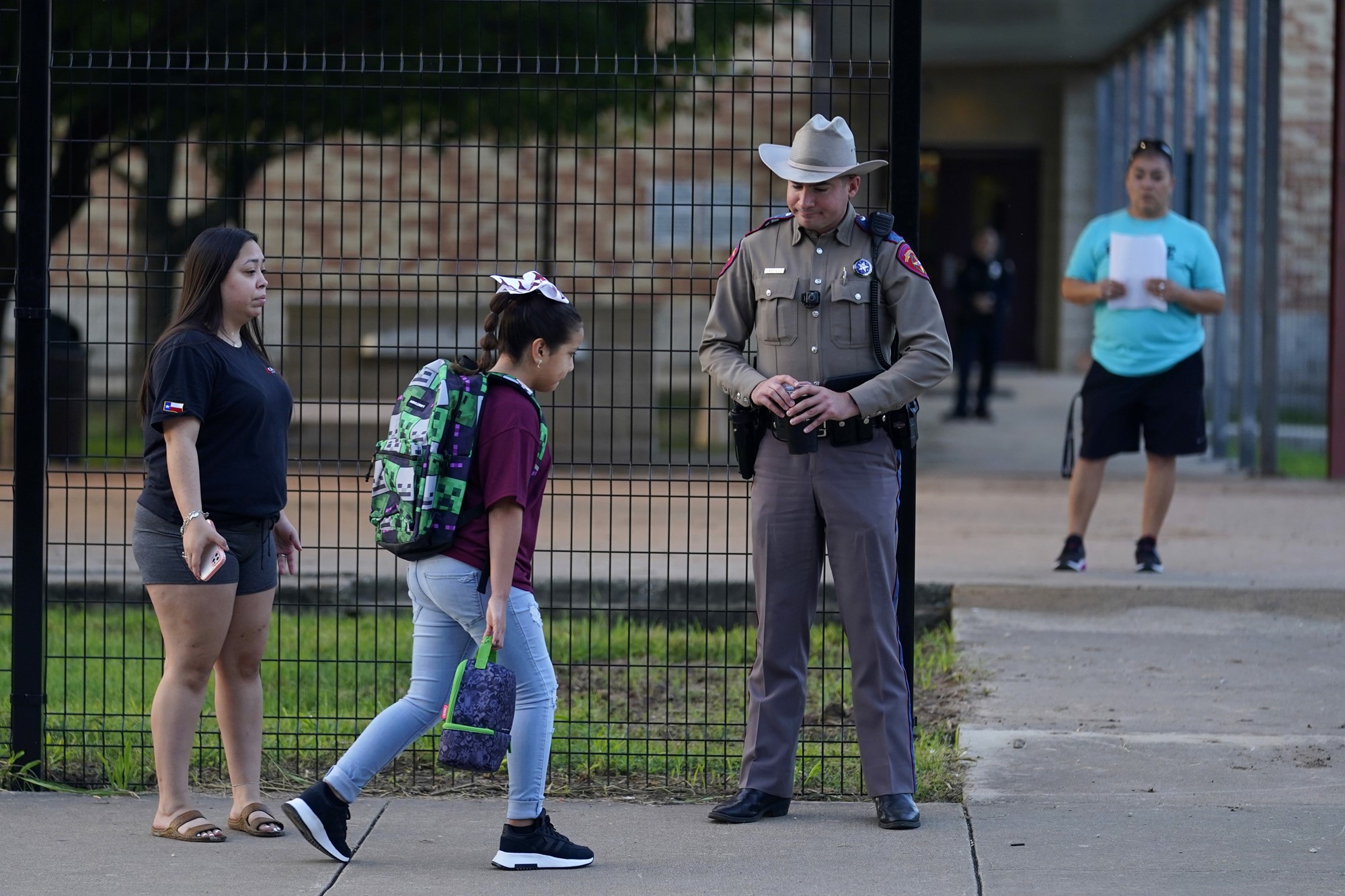 A young girl walks past a high fence and a gard into school