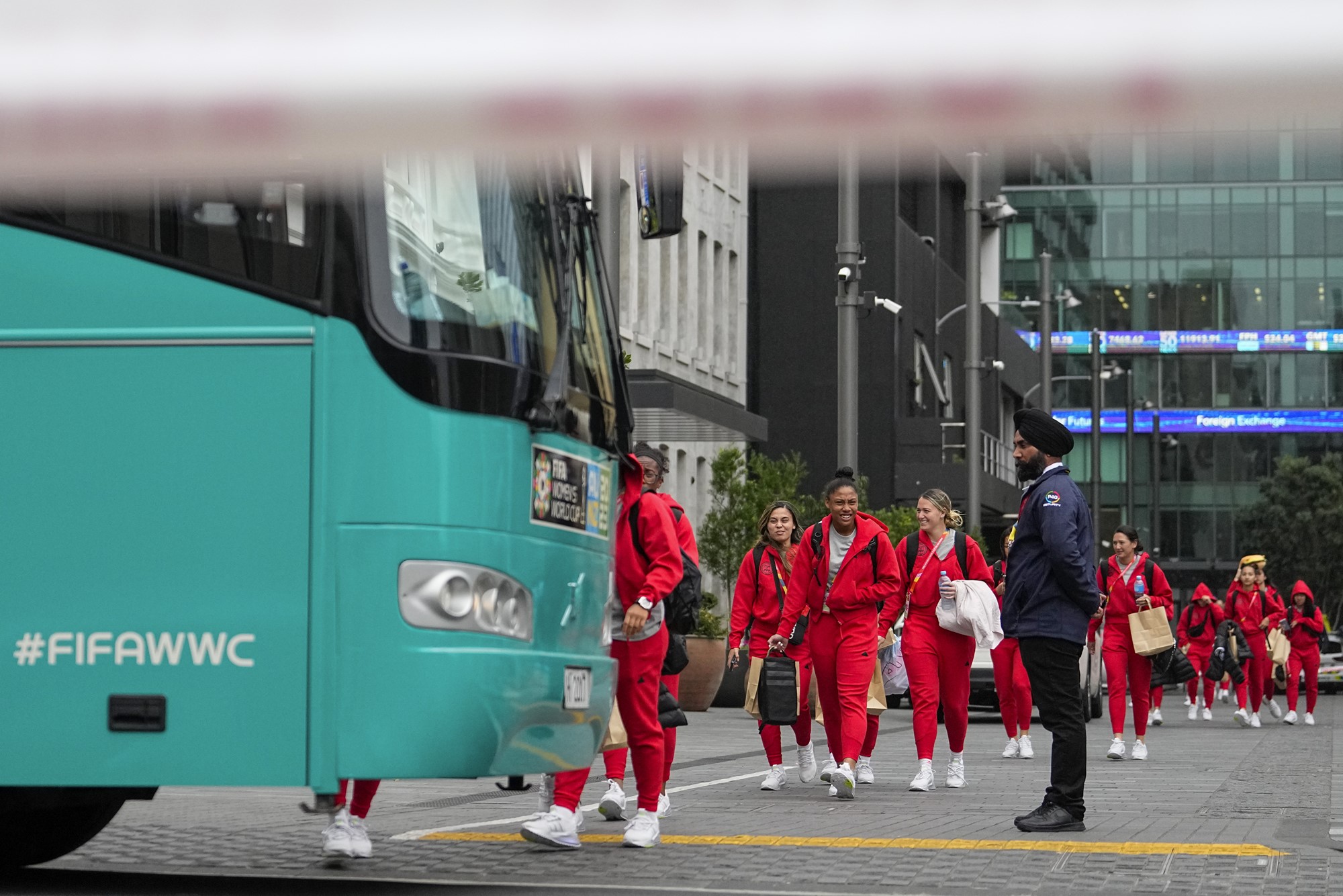 Around a dozen women in red track suits walk across the city centre onto a green bus marked FIFAWWC