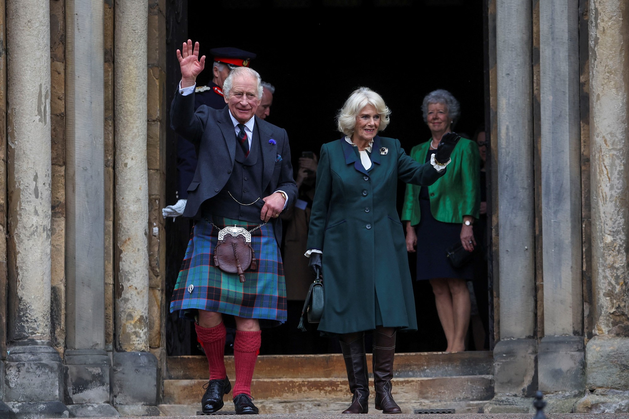 Charles, in a kilt and red knee high socks, waves with Camilla.