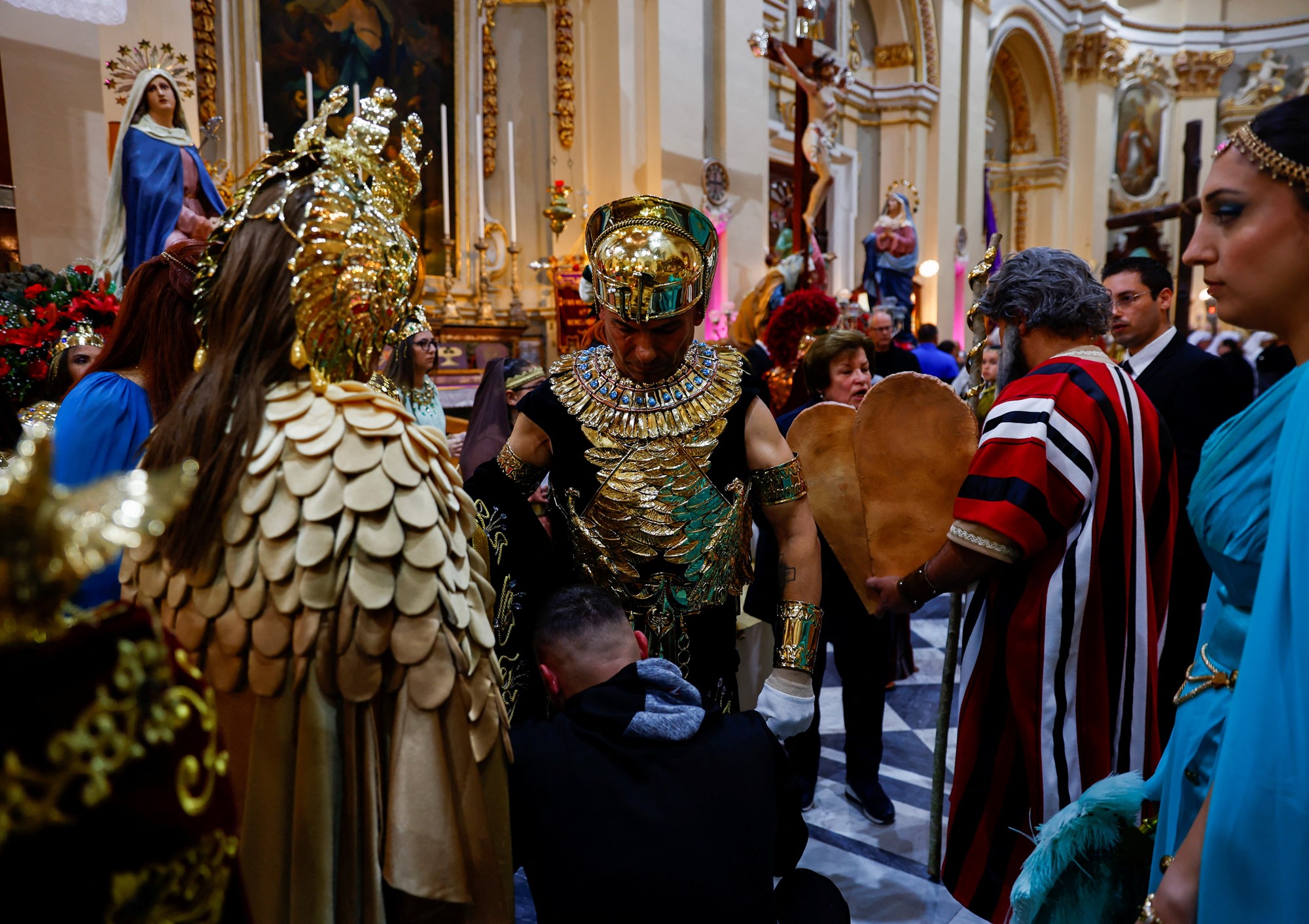 Two men dressed as Roman soldiers in gold armour stand amid a crowd in a church. 