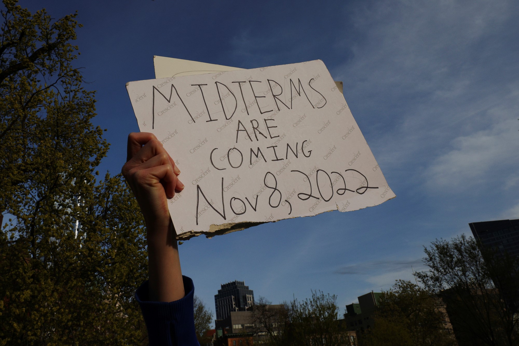 A ahnd holds a sign in the air that says "midterms are coming Nov 8 2022"